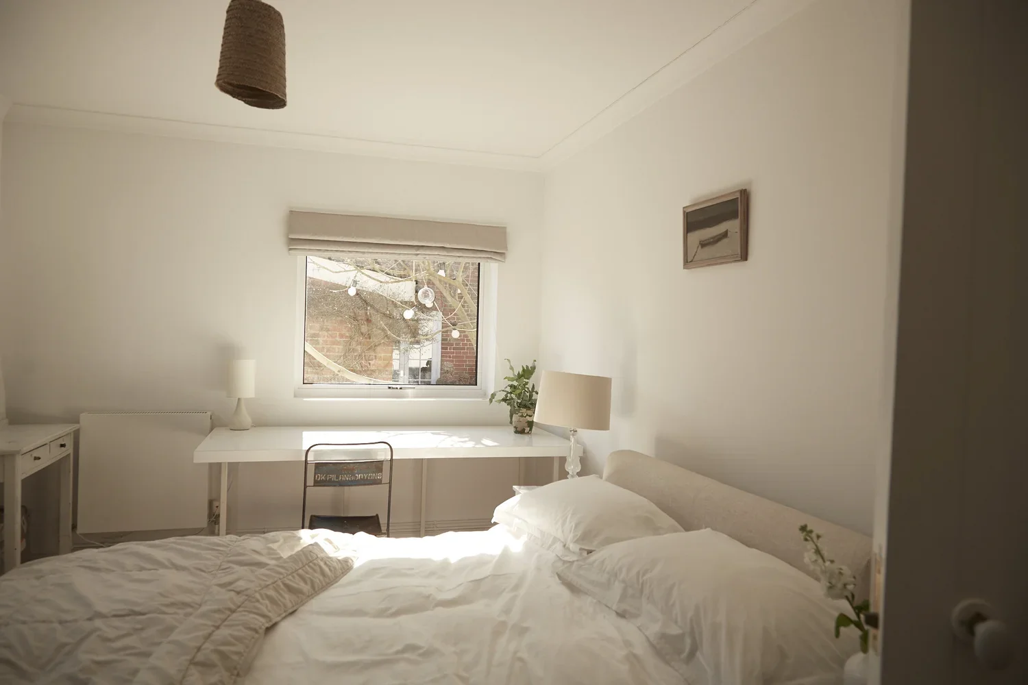 A bright bedroom with a bed, window, white walls, and simple furnishings