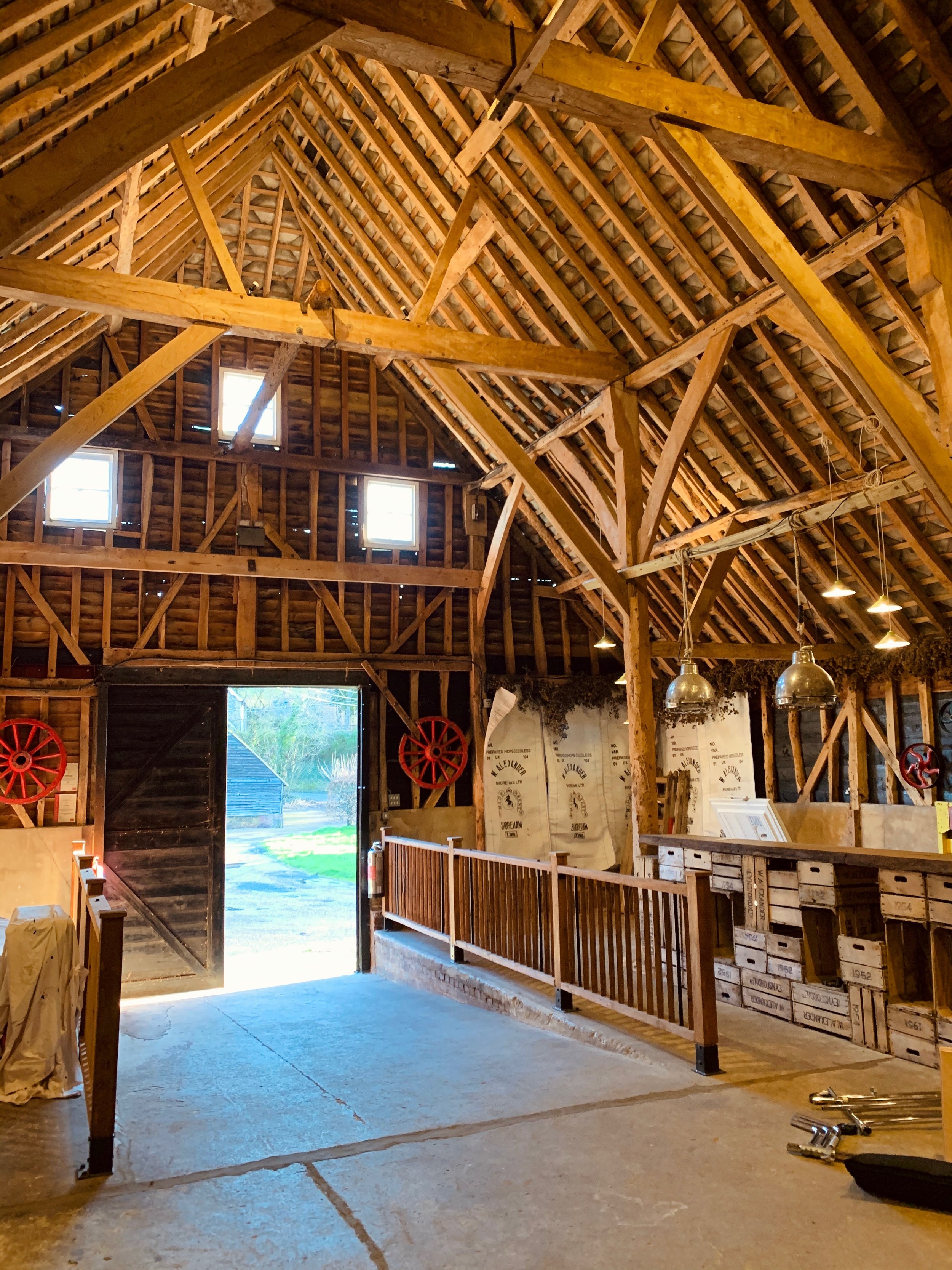 The image shows the interior of a barn or similar structure under construction with exposed wooden beams, some windows, hanging light fixtures, and building materials on the floor.