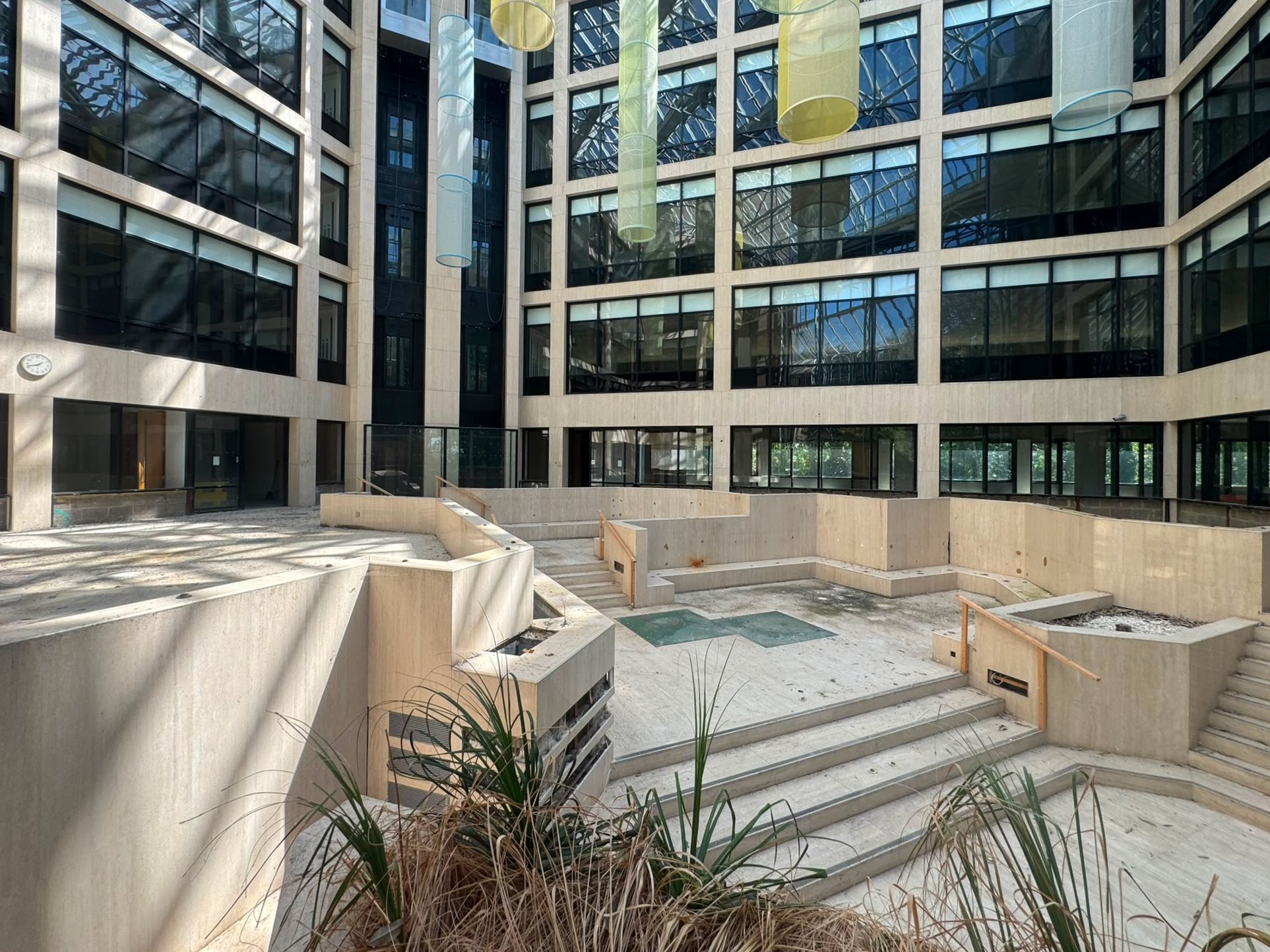 The interior courtyard of a modern building under construction, with concrete stairs, plants, and large glass windows.