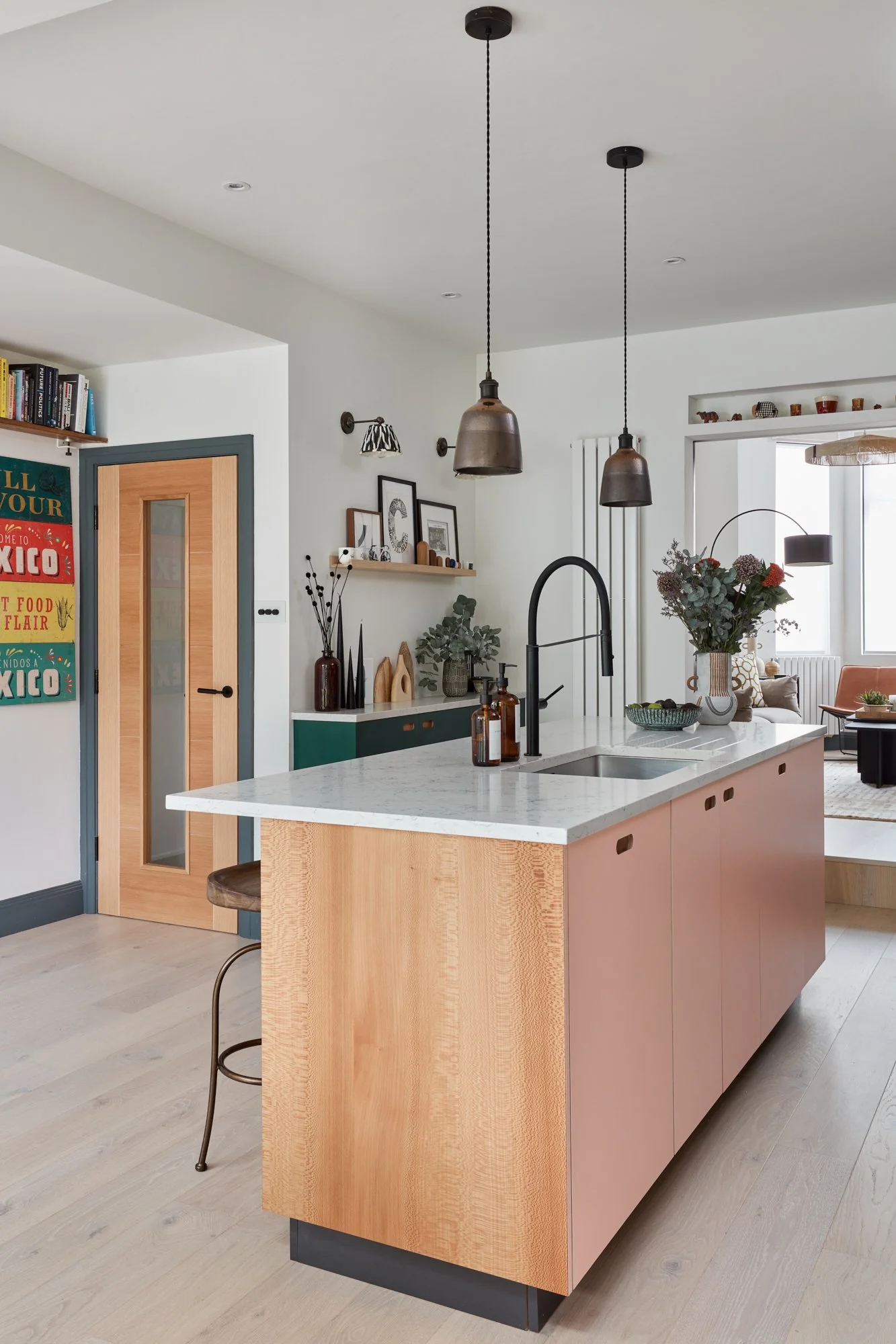 Modern kitchen with light wood cabinets, white marble countertop, black faucet, copper pendant lights, decorative wall shelves, and a vase with flowers.