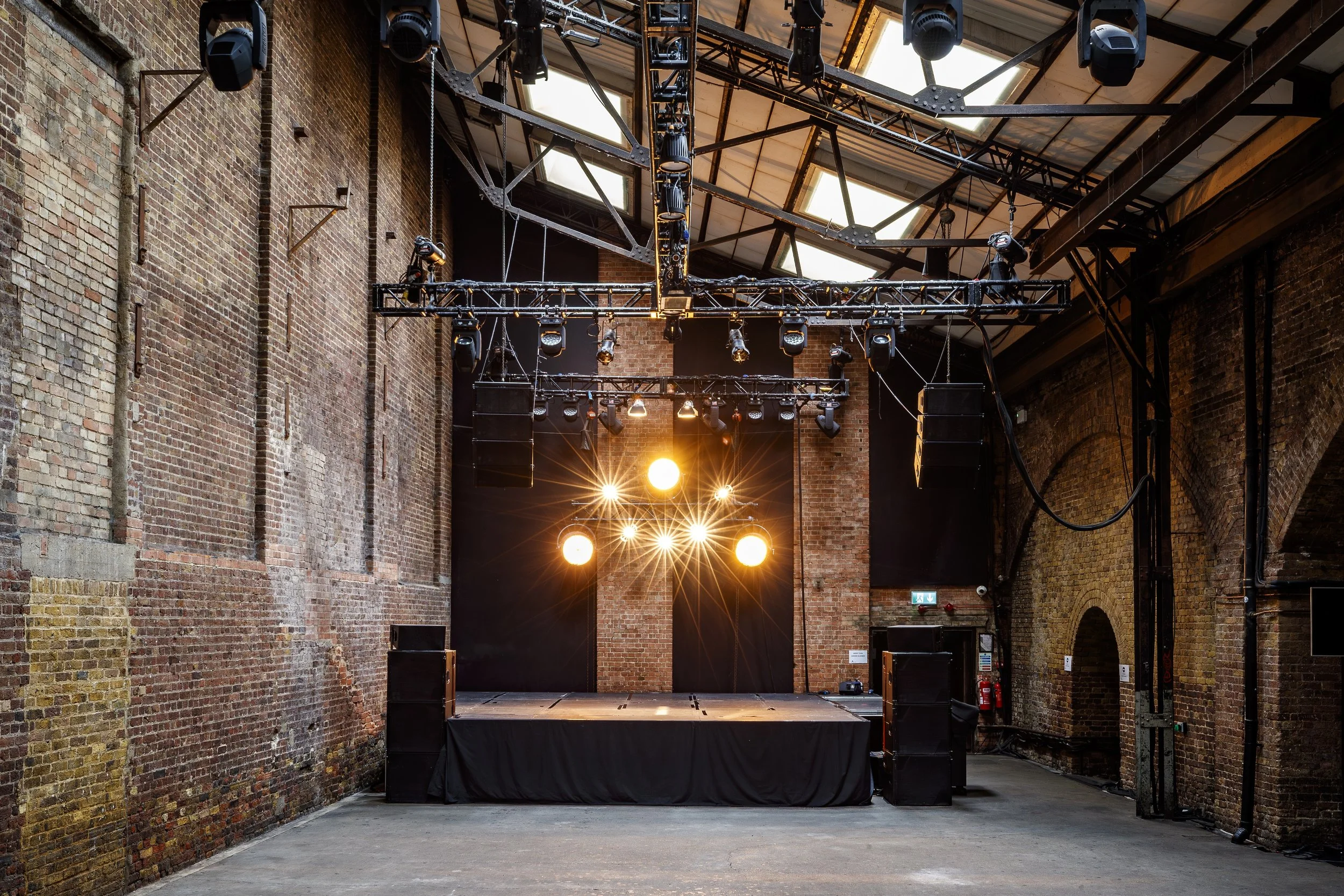 Empty stage setup in an industrial brick building with stage lights and speakers, ready for a performance or event.
