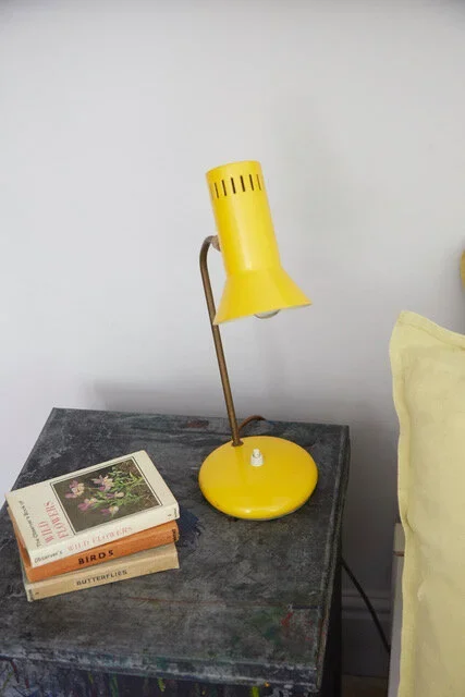 Yellow desk lamp on a dark wooden table next to a stack of books and a yellow pillow.