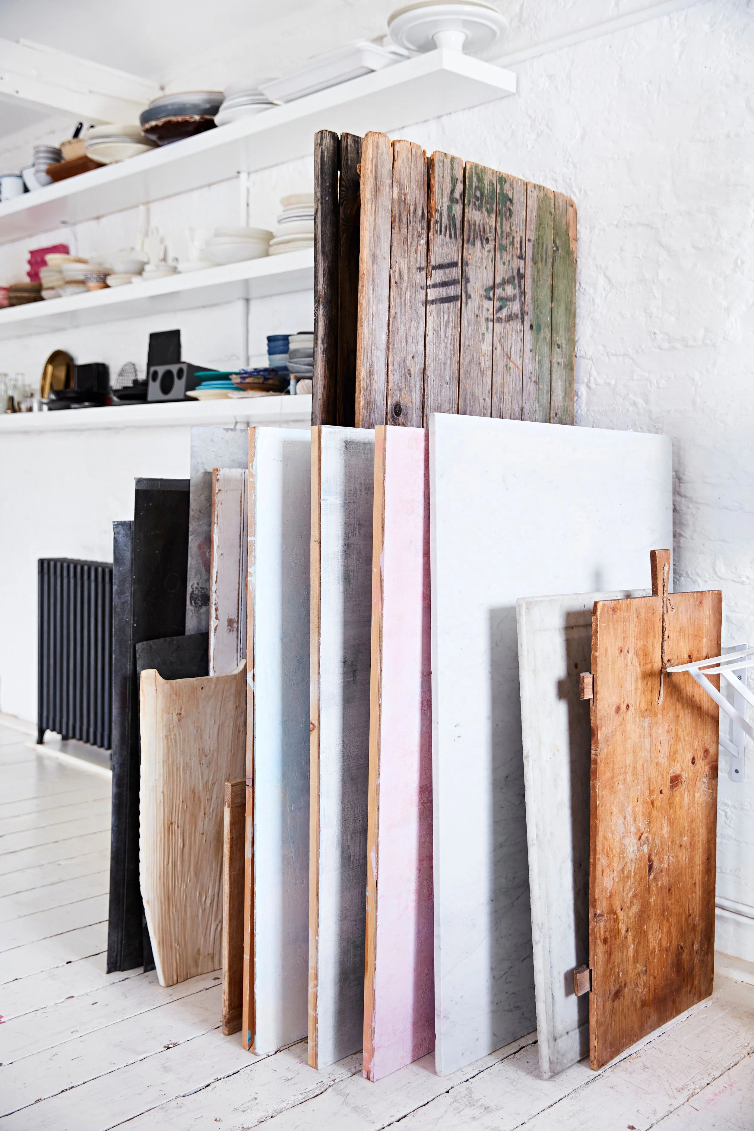 Clack of wooden and stone slabs leaning against a white wall in a bright kitchen or studio.