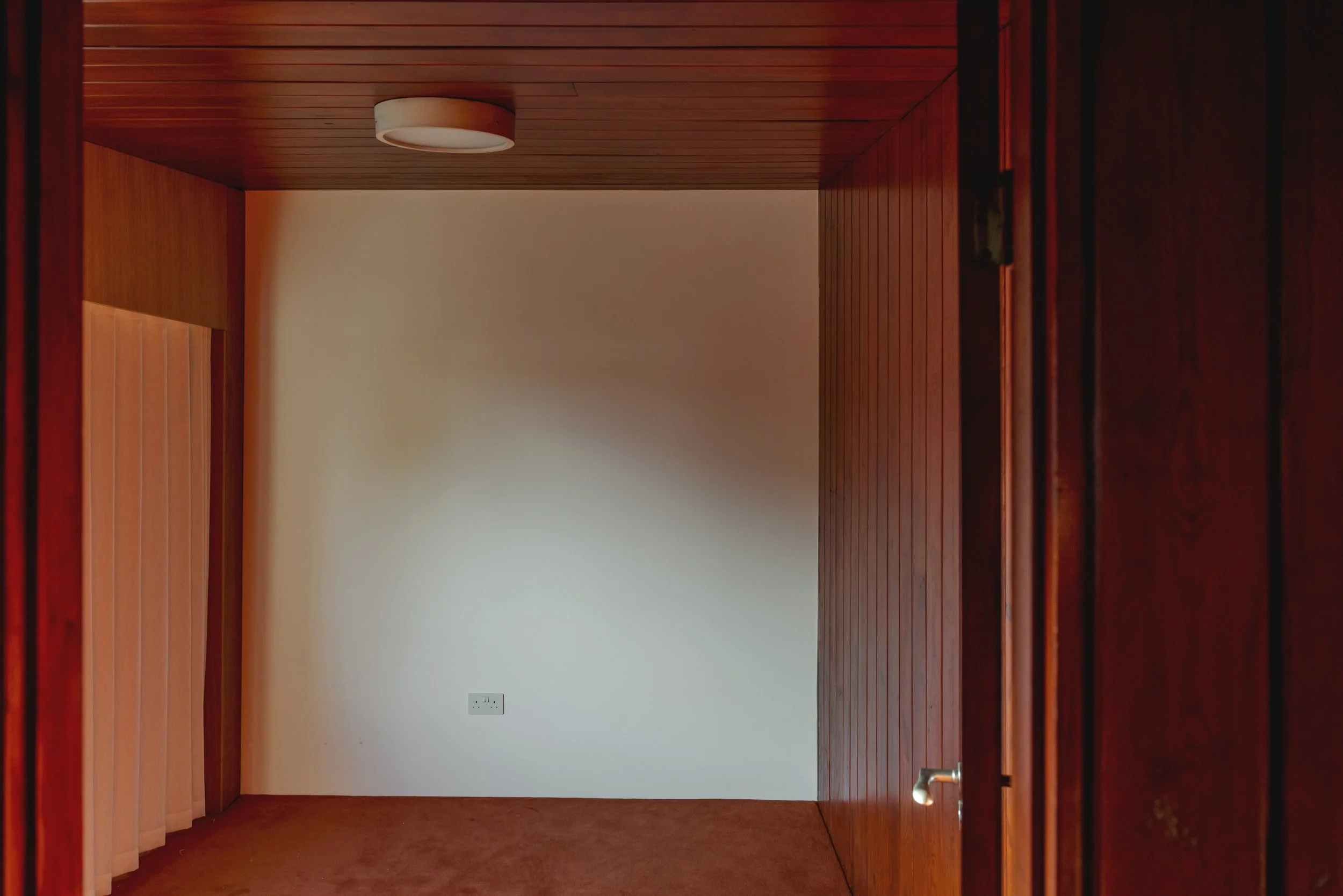Empty room with wood-paneled walls and ceiling, white wall with electrical outlet, and a closed door.