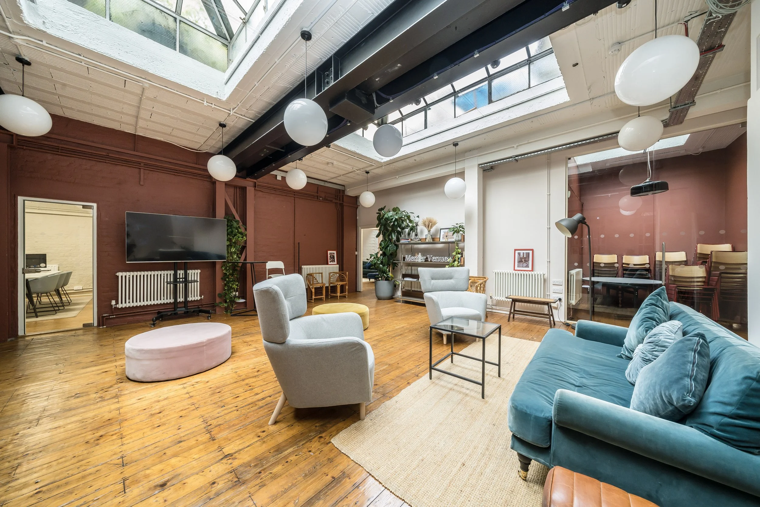 Bright and modern living room with wooden floors, white and blue seating, large window ceiling, and a glass partition over a space with stacked chairs.