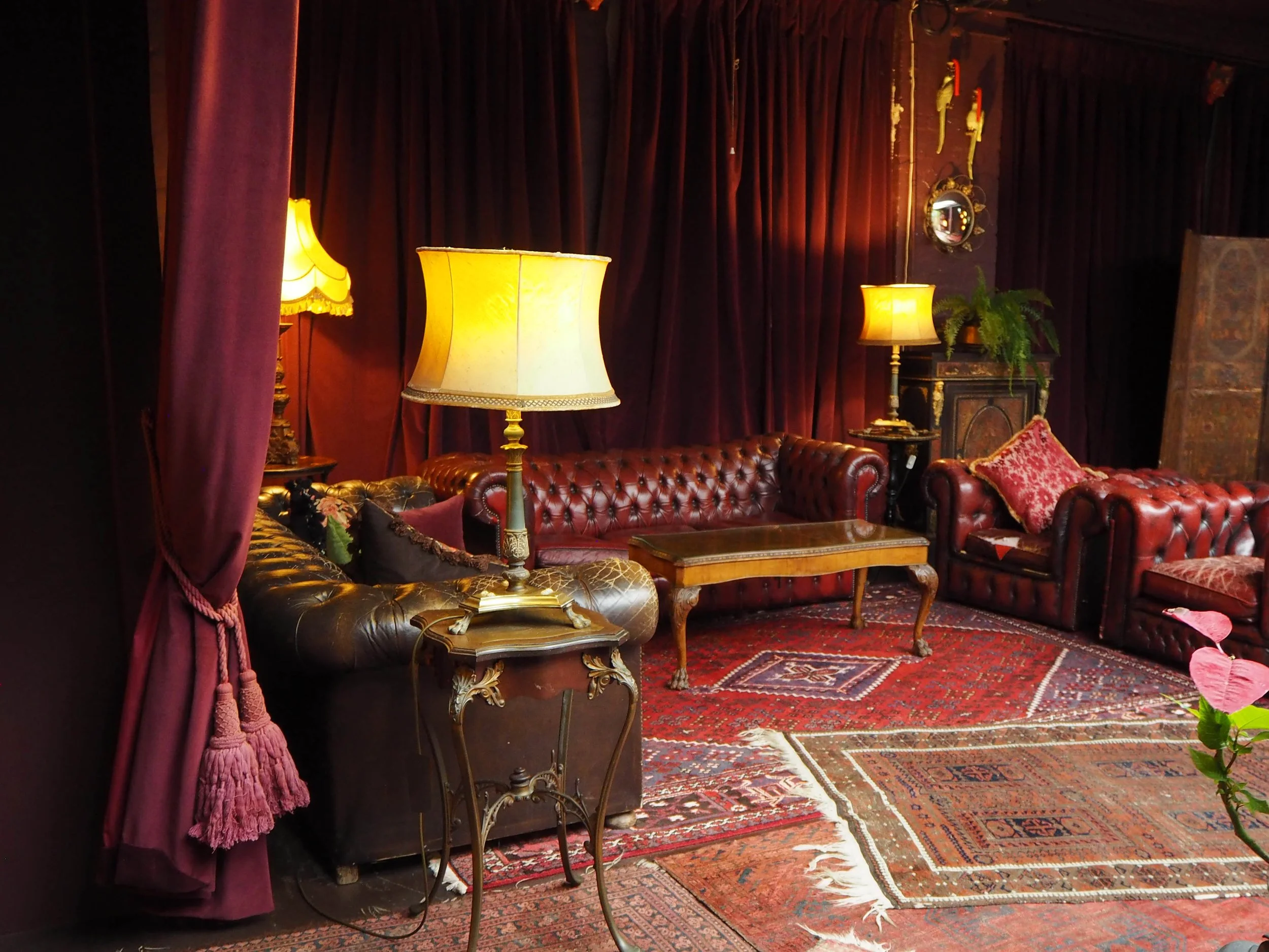 A cozy living room with red velvet curtains, vintage leather sofas, decorative rugs, and warm yellow lamps creating a vintage ambiance.