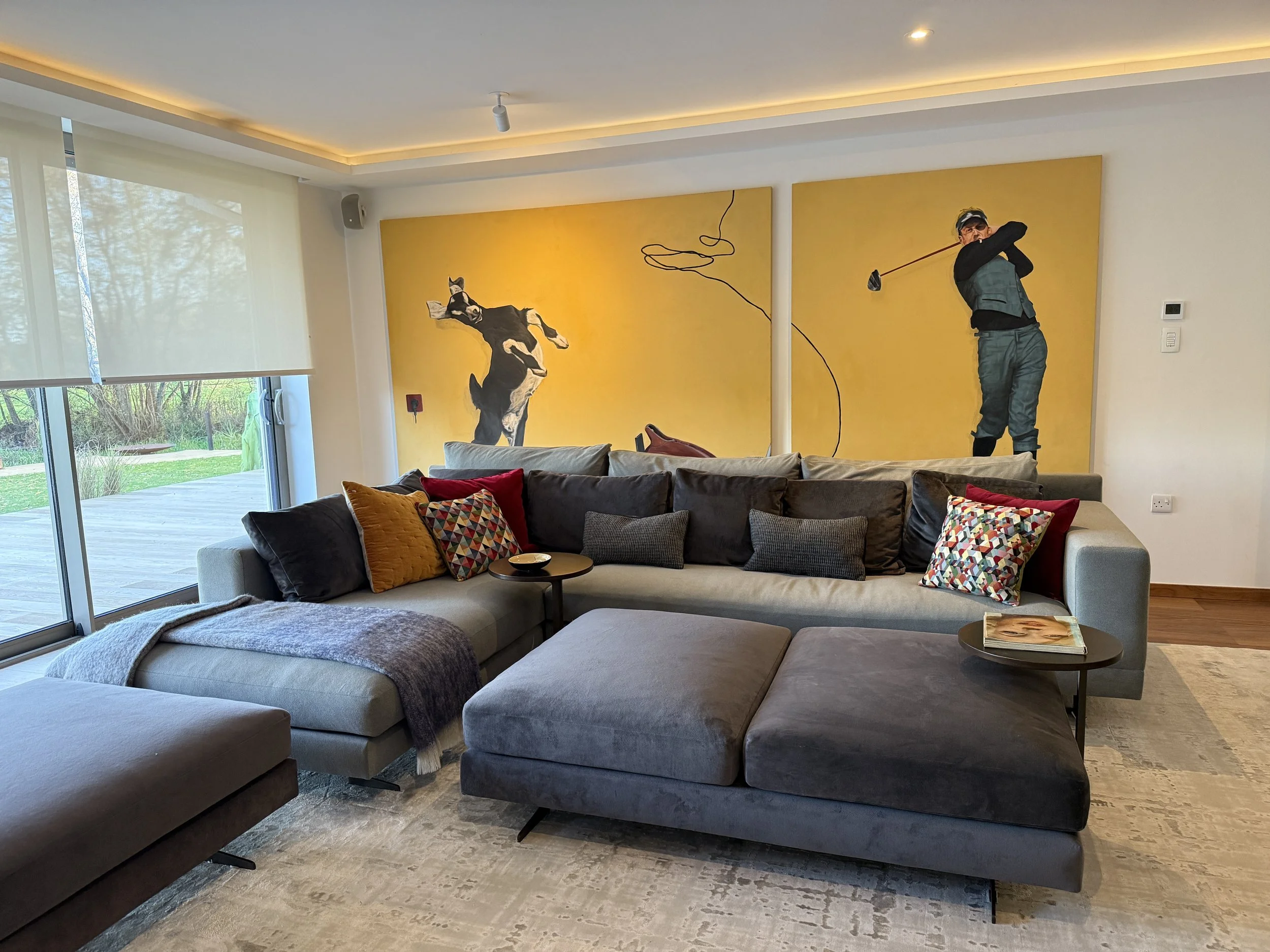 Living room with a large sectional sofa, colorful patterned and solid pillows, and a wall mural of a dog and a man playing golf.