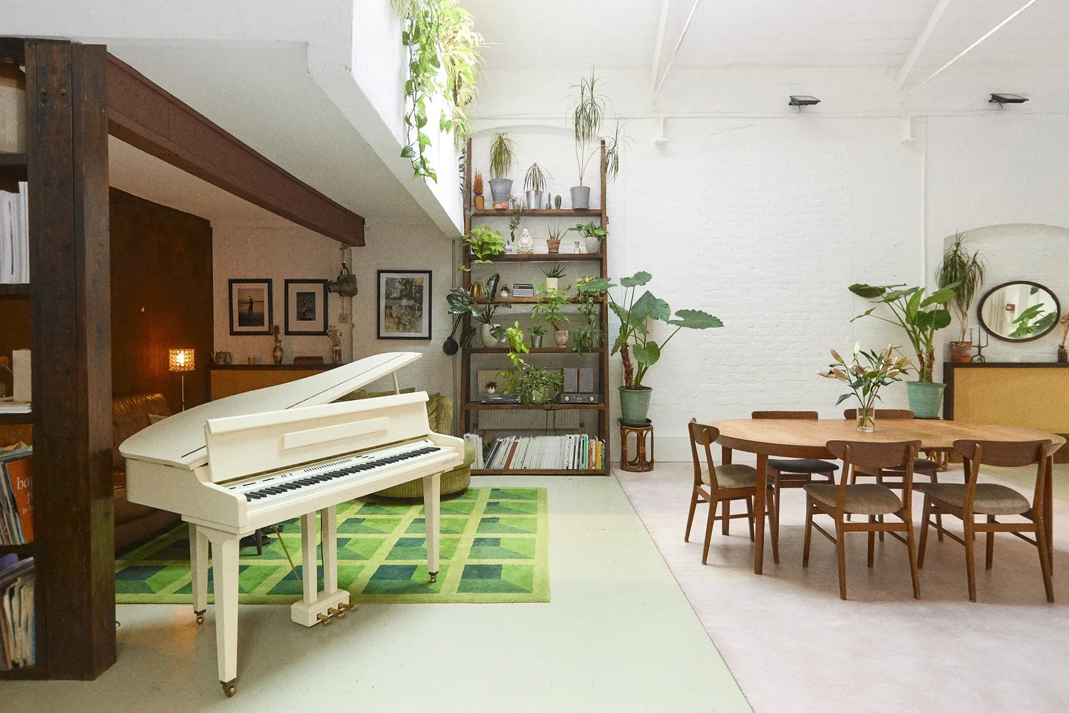 Living space with a white piano, green rug, wooden dining table with six chairs, and numerous potted plants on shelves and surfaces.