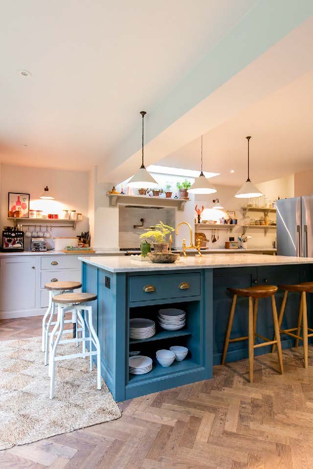 Bright kitchen with a blue island, white countertops, open shelves with dishes and decor, and wooden stools.