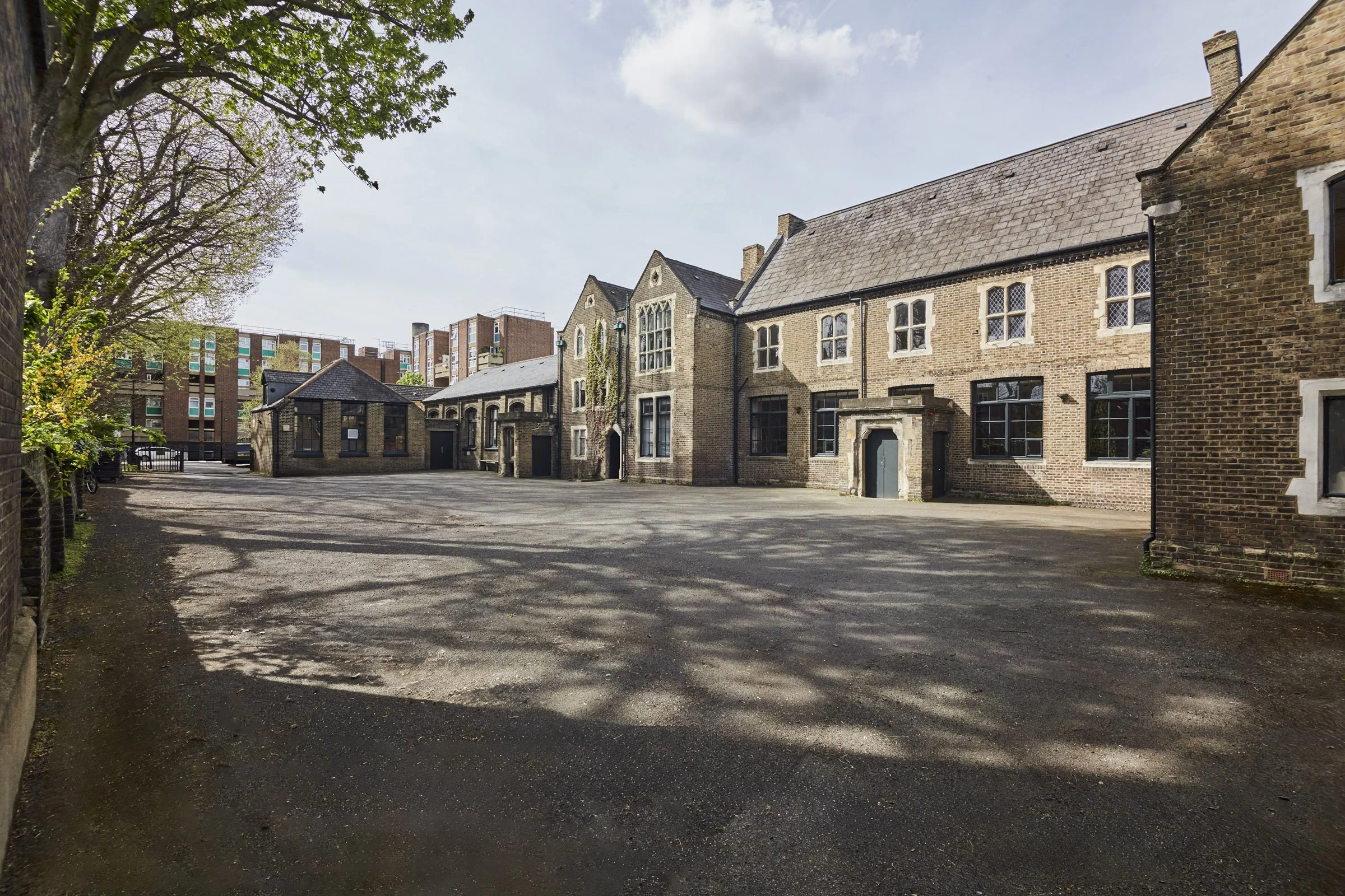 A historical brick building with a large courtyard, surrounded by trees and shadows.