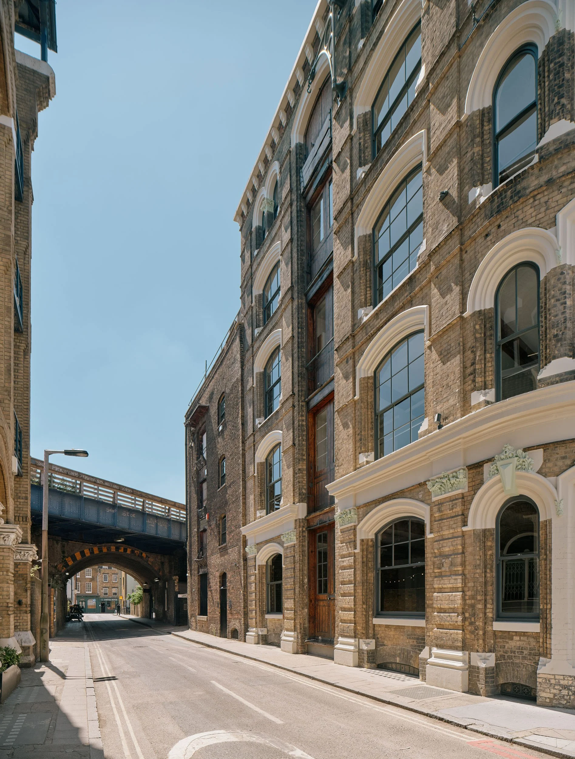 Empty city street lined with historic brick buildings, with an underpass in the background and clear blue sky.
