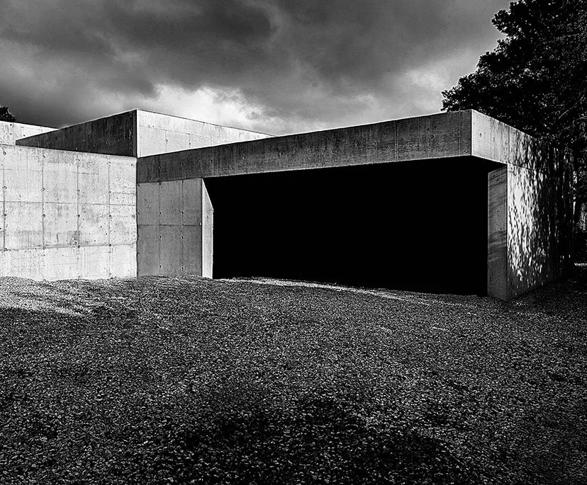 Modern concrete structure with a large rectangular opening, set against a dark, cloudy sky.