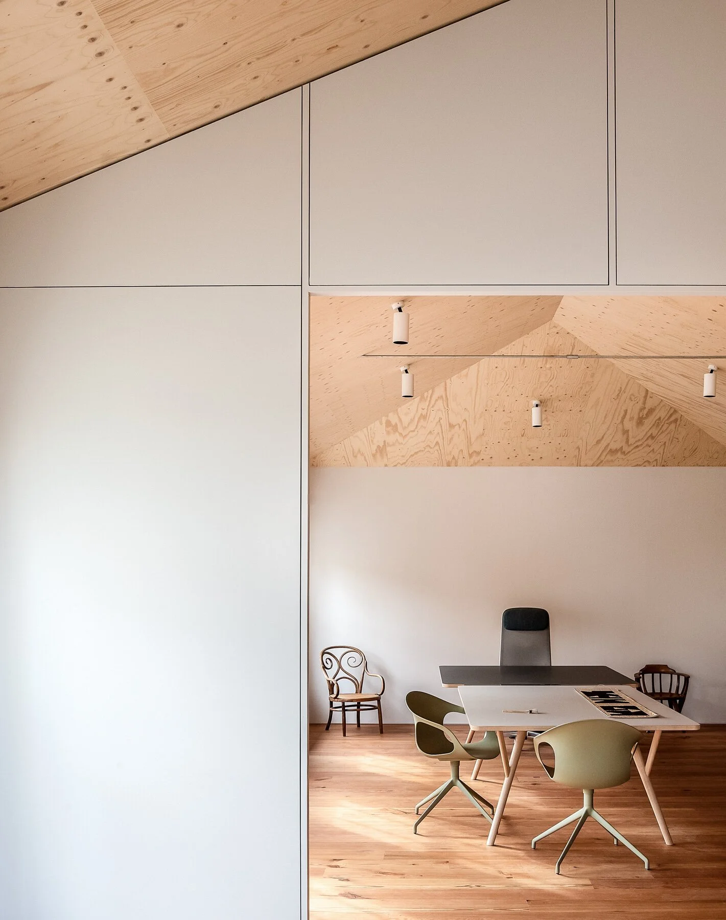 Minimalist office with a white table, several chairs, and a gray office chair, in a room with wooden ceiling and floor, and white walls.