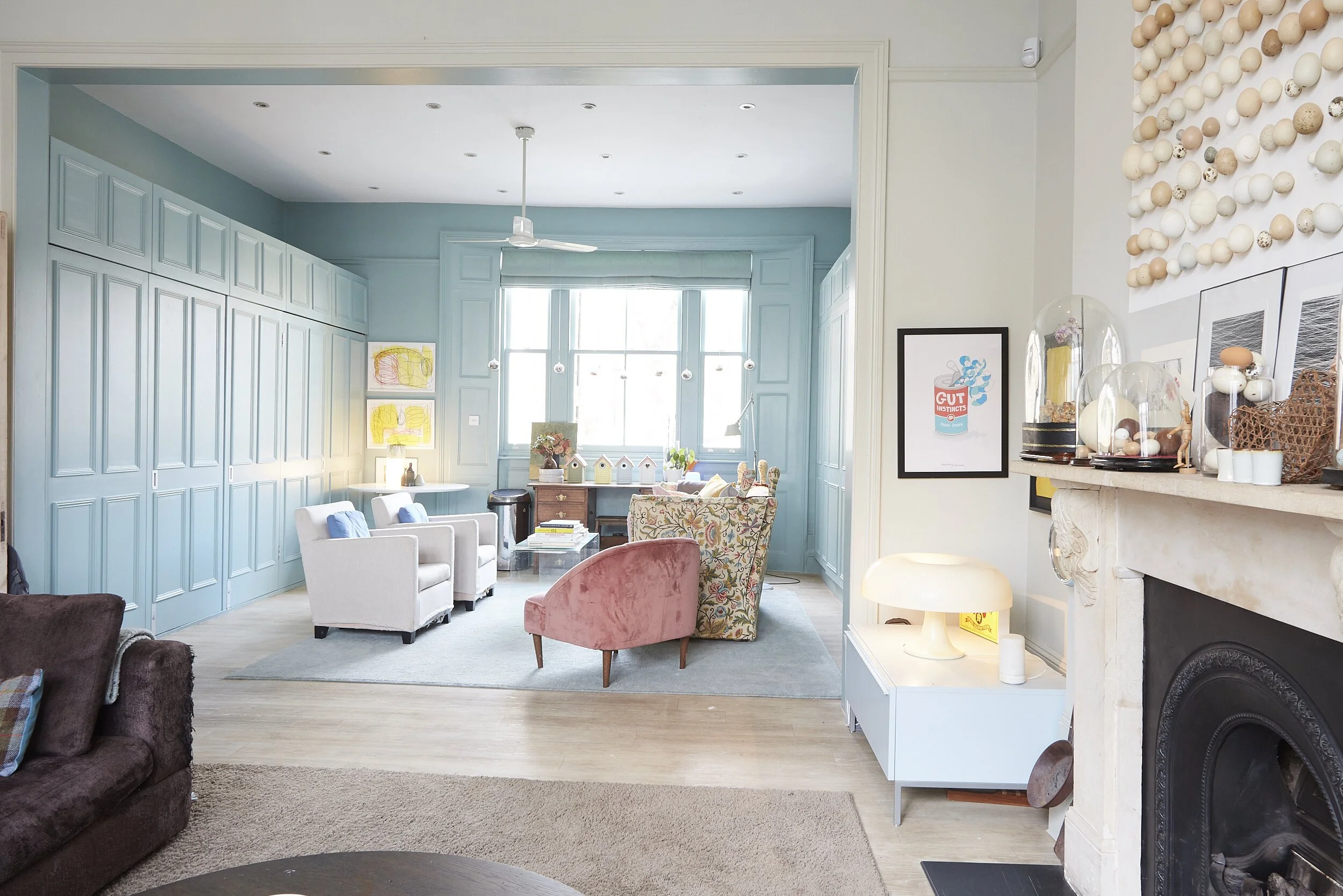 Living room with a blue paneled wall, large window, chairs, a fireplace, and decorative items.