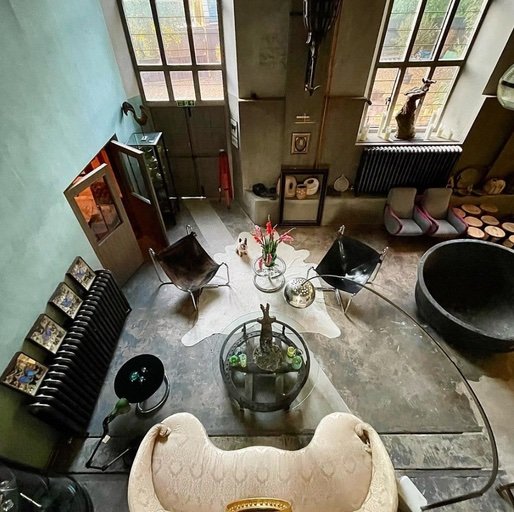 Top-down view of a living room with large windows, a mix of modern and vintage furniture, a black round bowl, a sofa, and various decorative items.