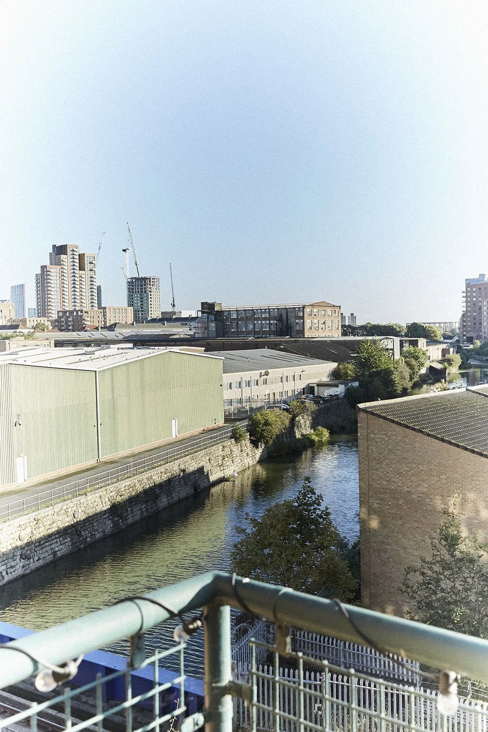 Cityscape with industrial buildings, a river, and skyscrapers in the background.