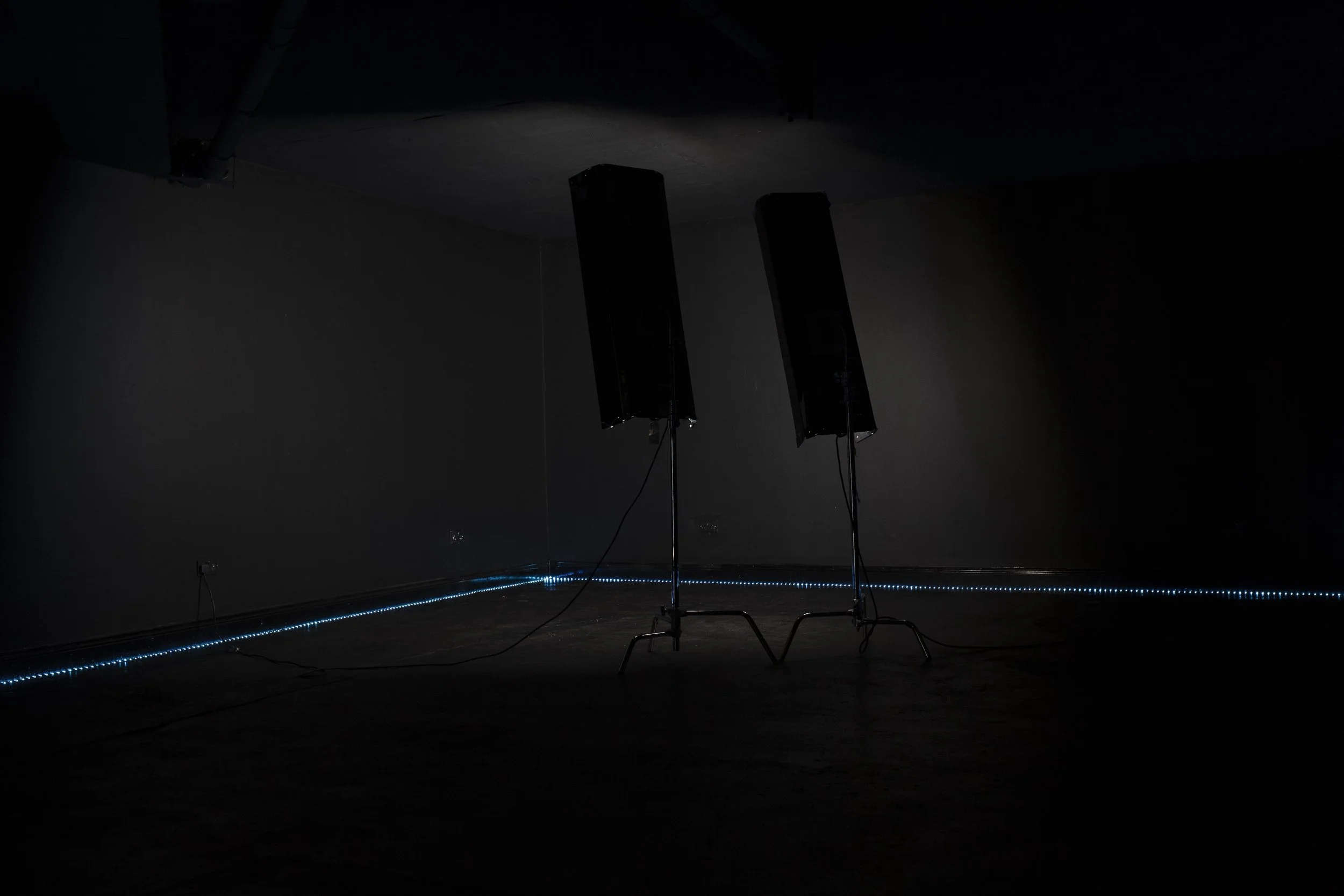 Dark room with two standing speakers and a strip of blue LED lights along the floor.