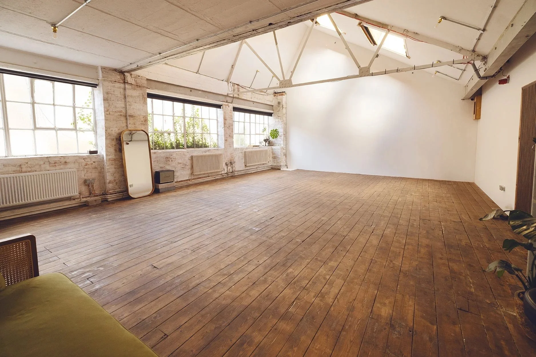 Spacious empty room with large windows, wooden floor, exposed brick wall, and ceiling beams.