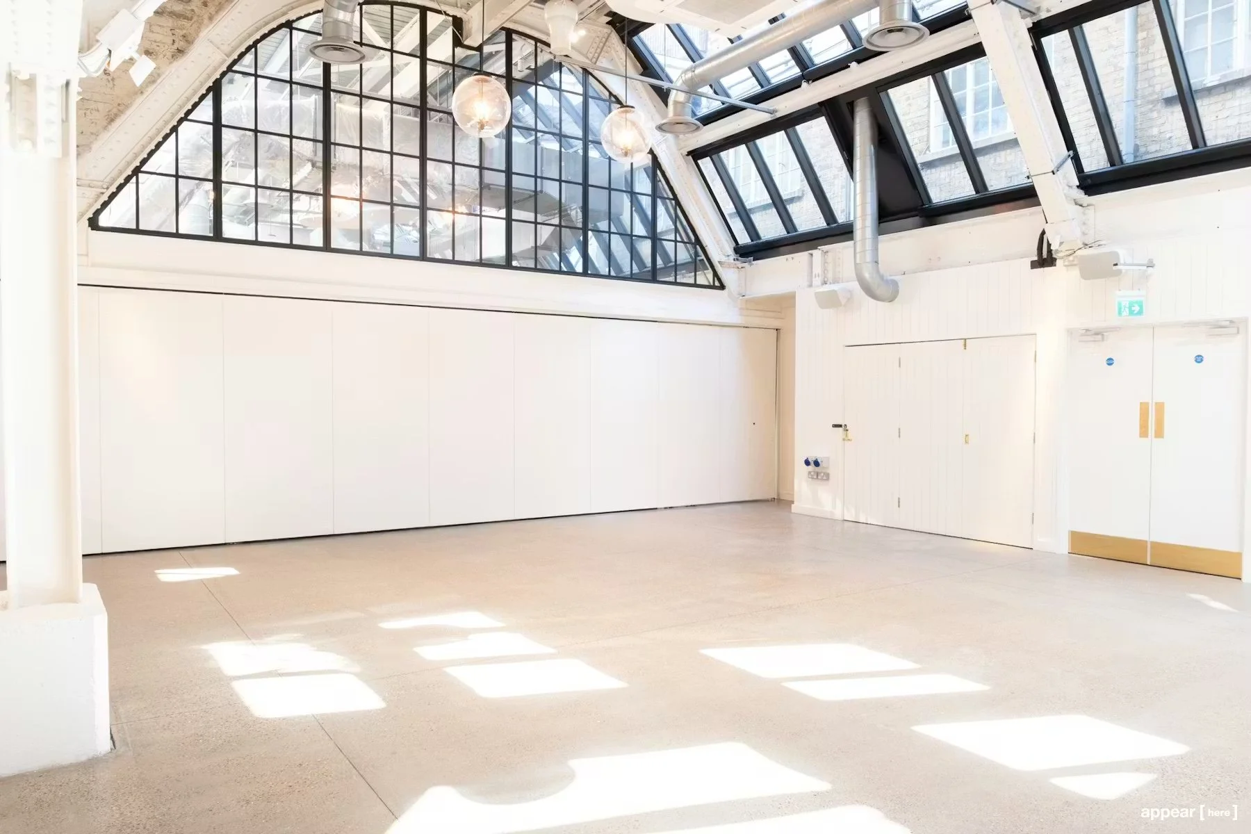 Empty bright room with white walls, large windows, and skylights, allowing sunlight to cast square-shaped light spots on the floor.