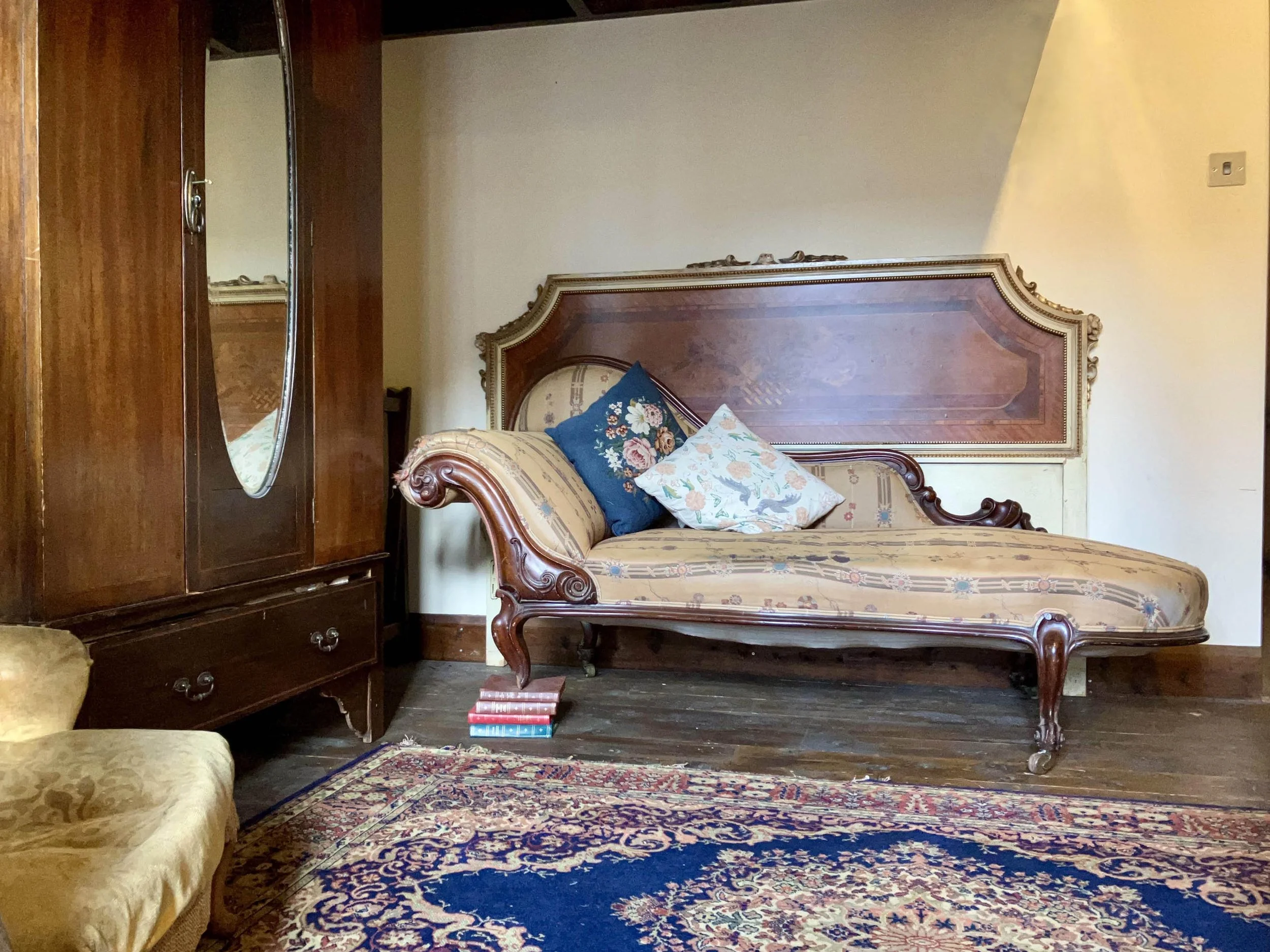 Vintage living room with an ornate wooden daybed, a wooden wardrobe with a mirror, a yellow upholstered chair, and a patterned rug.