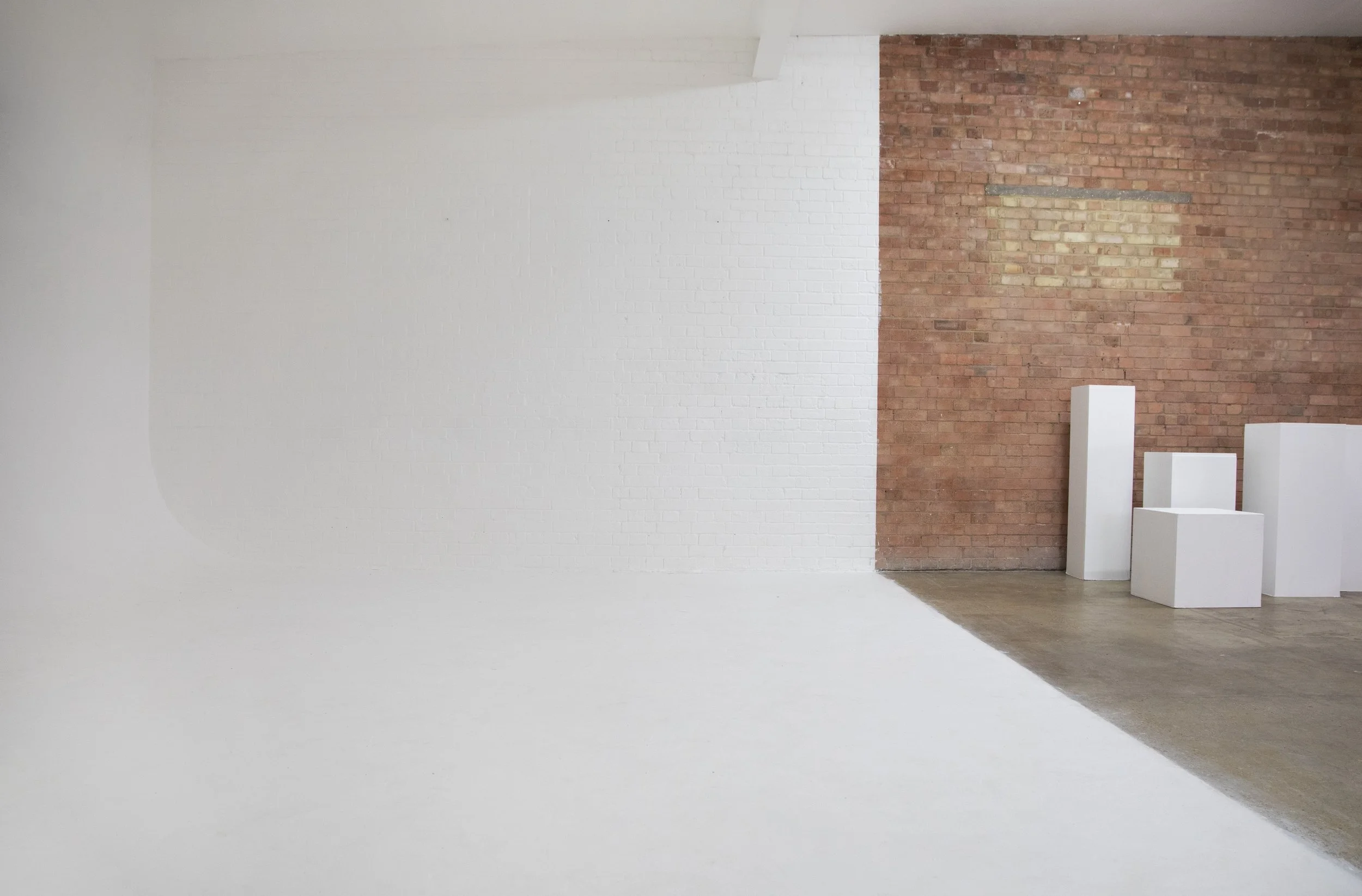 Empty art gallery with white and brick walls and four white display pedestals.