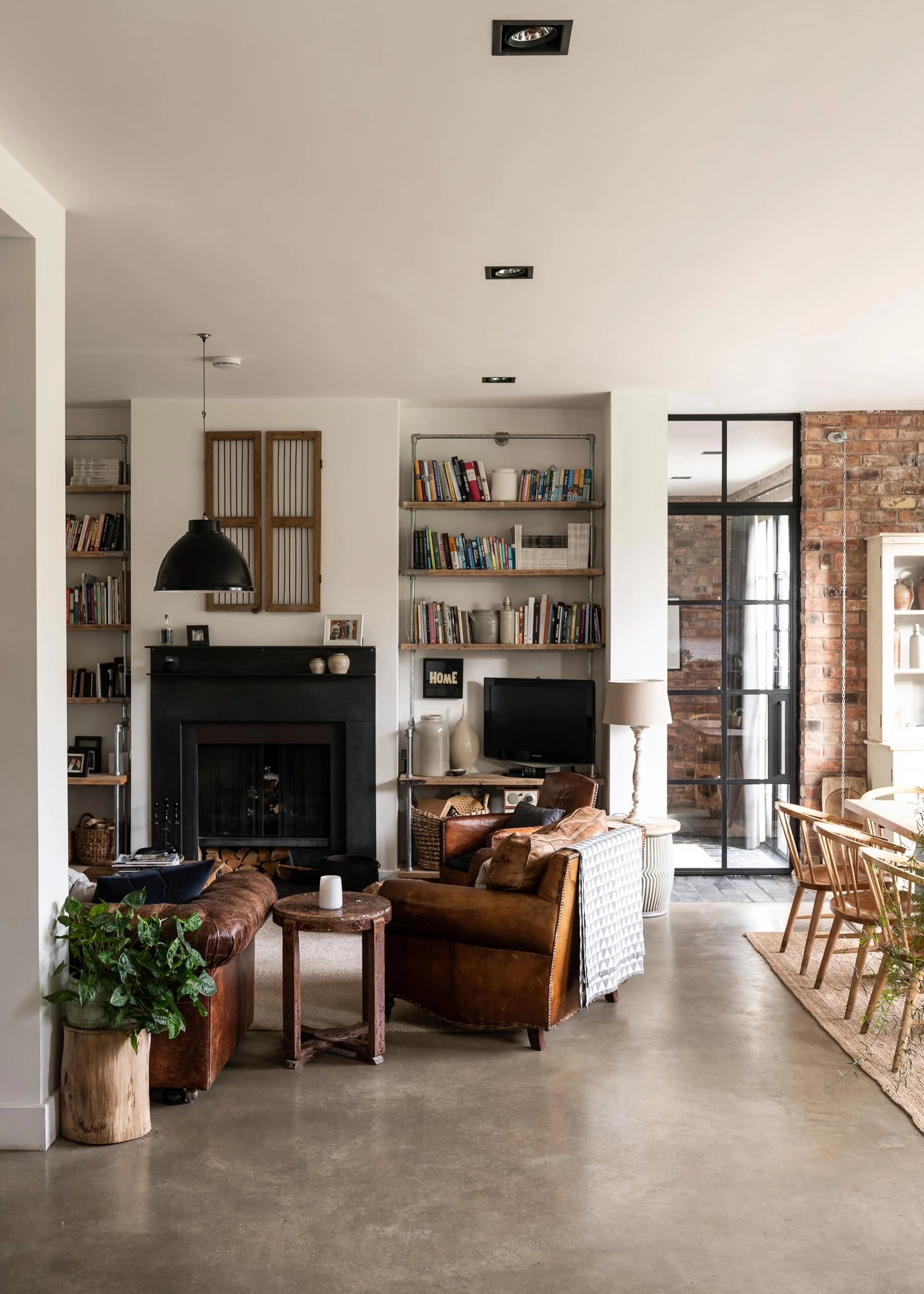 Living room with leather sofas, a wooden coffee table, a fireplace, bookshelves, a small TV, and a sliding glass door leading outside.