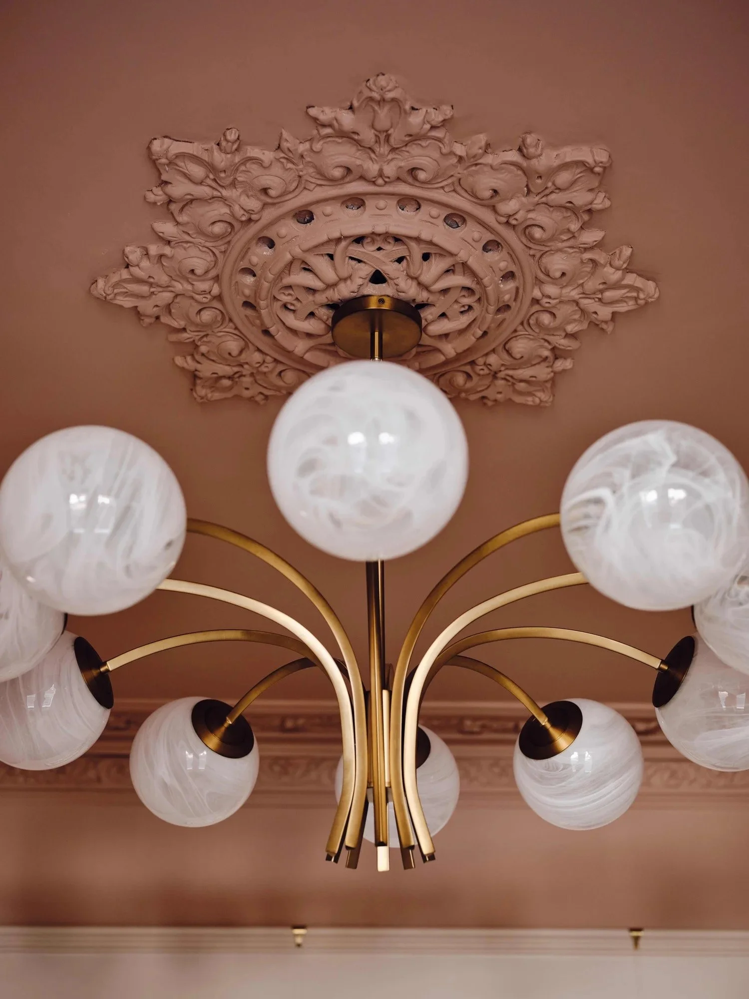 Elegant chandelier with multiple white marbled glass globes hanging from gold arms, mounted on a decorative ceiling medallion in a classic room.