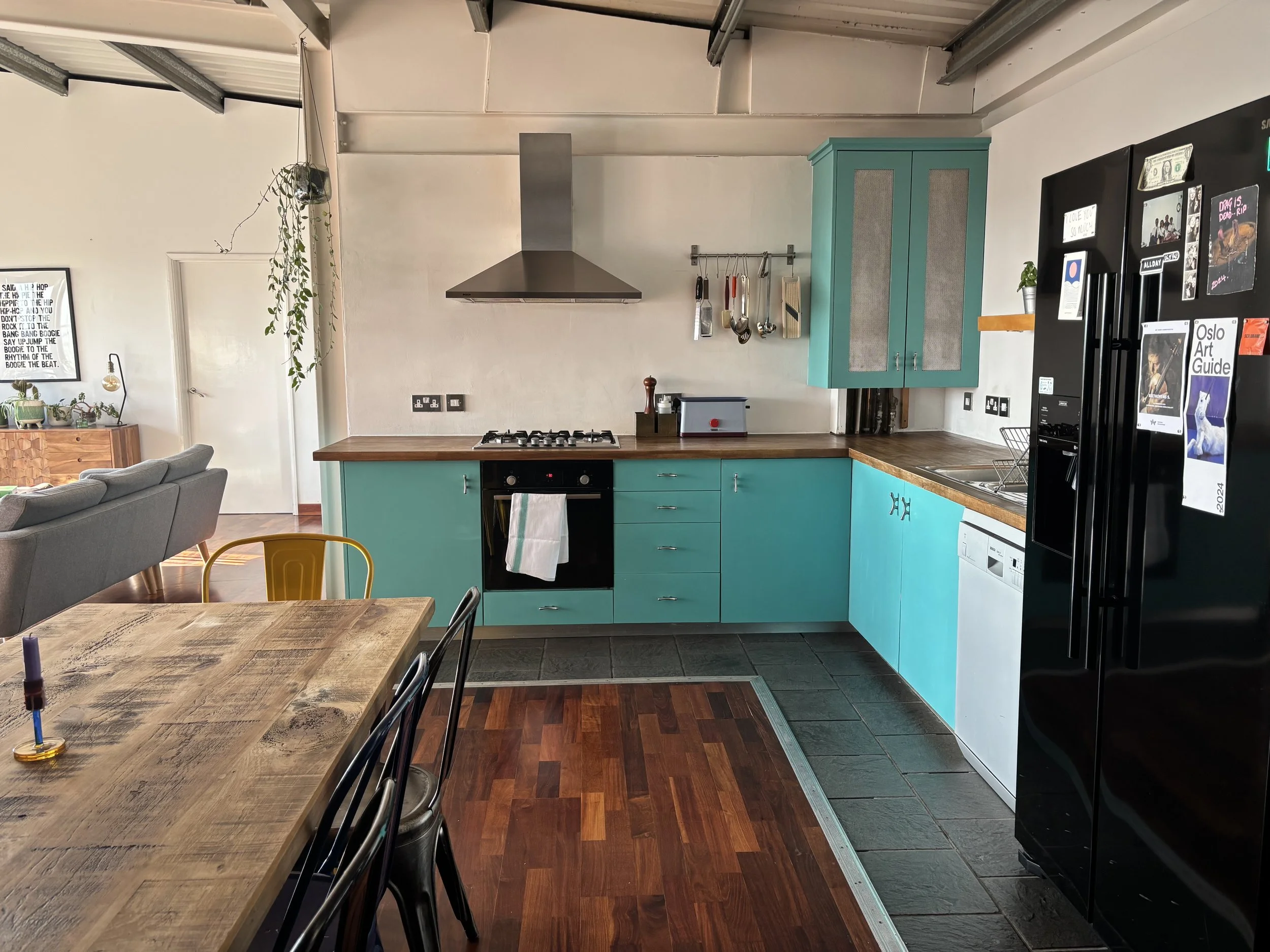 Kitchen with teal cabinets, wooden countertops, black appliances, and a dining table with black chairs.