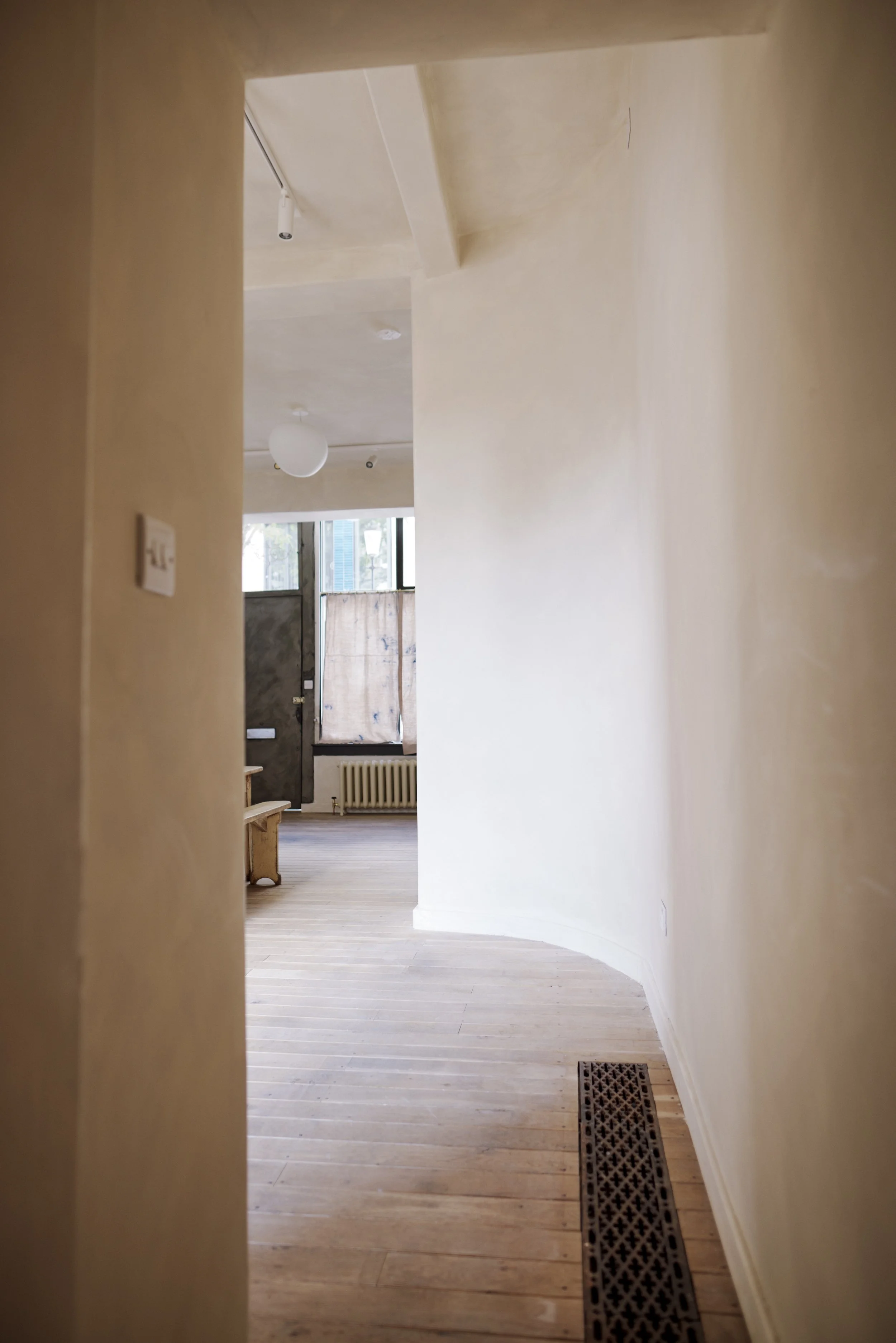 Interior view of a hallway leading to a room with wooden floors, a radiator, and a window with a makeshift cover.