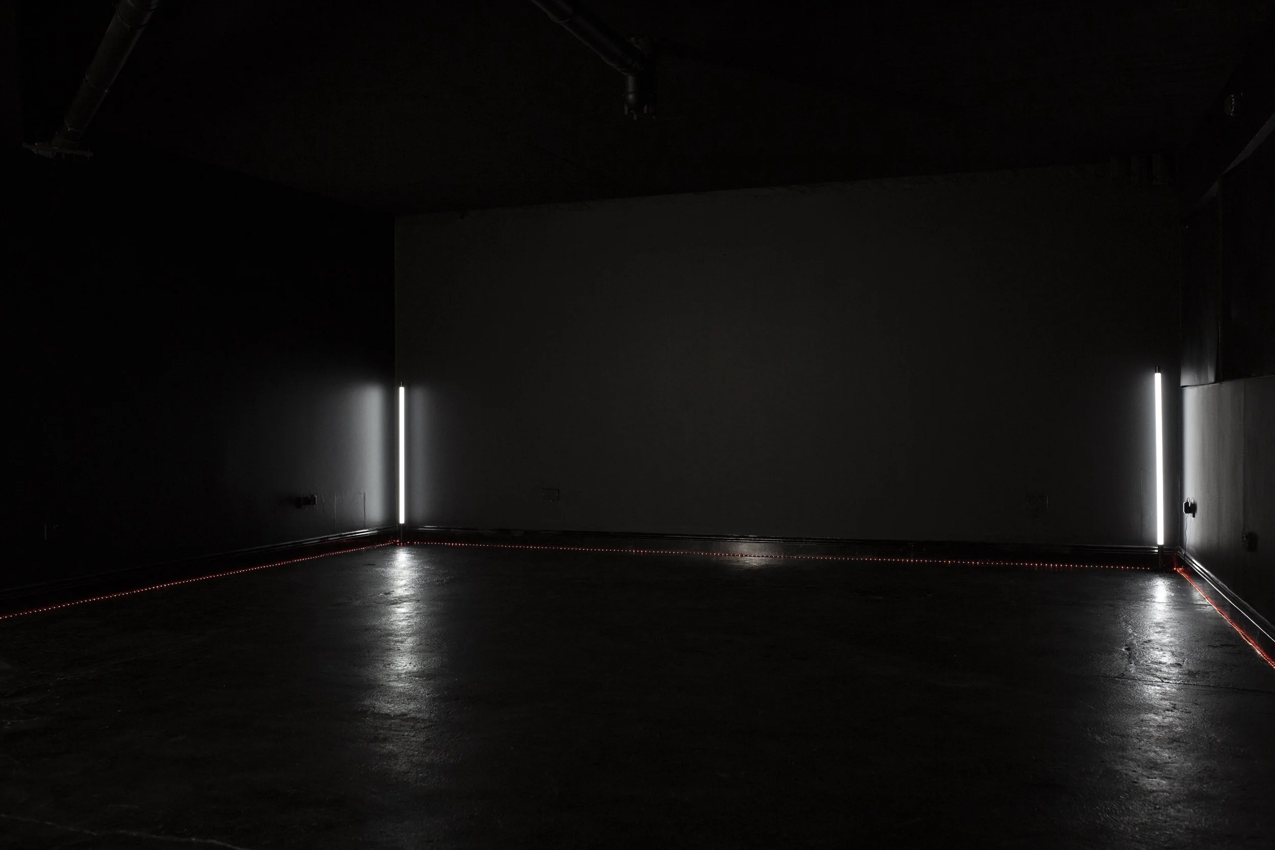 Dark room with vertical white light strips on adjacent walls and red LED strips along the floor corners.