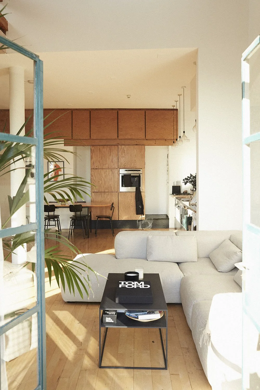Living room with white sectional sofa, black coffee table with Tommy Hilfiger shopping bag, and potted plant near a blue window frame.