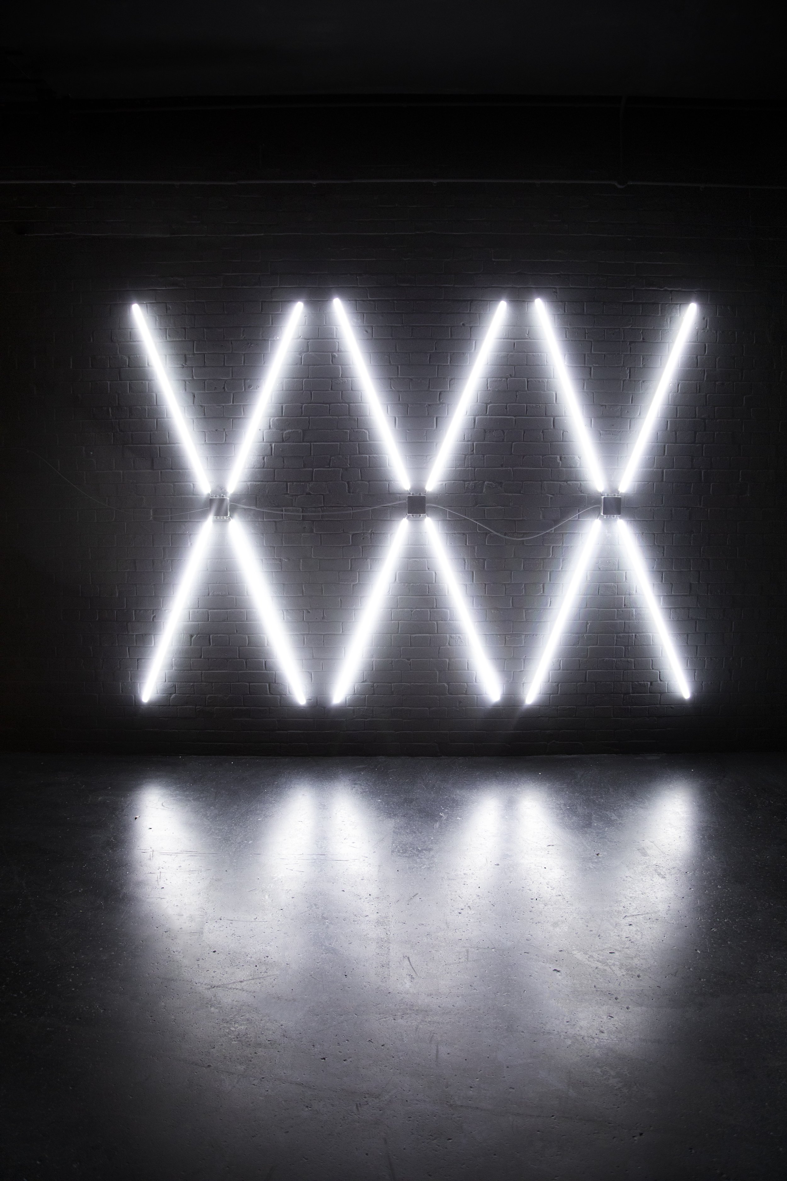 Neon wall art with white light tubes arranged in a zigzag pattern on a dark wall, reflecting on the floor.