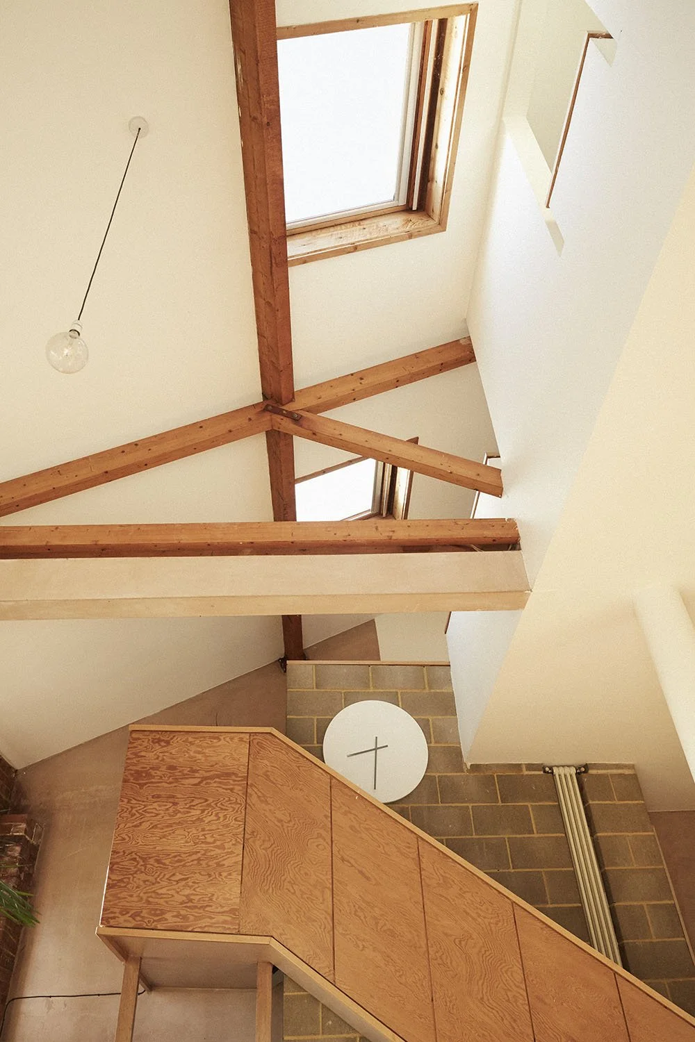 Interior view of a modern home with exposed wooden beams, skylights, and a staircase. There is a clock on the wall with a minimalist design.