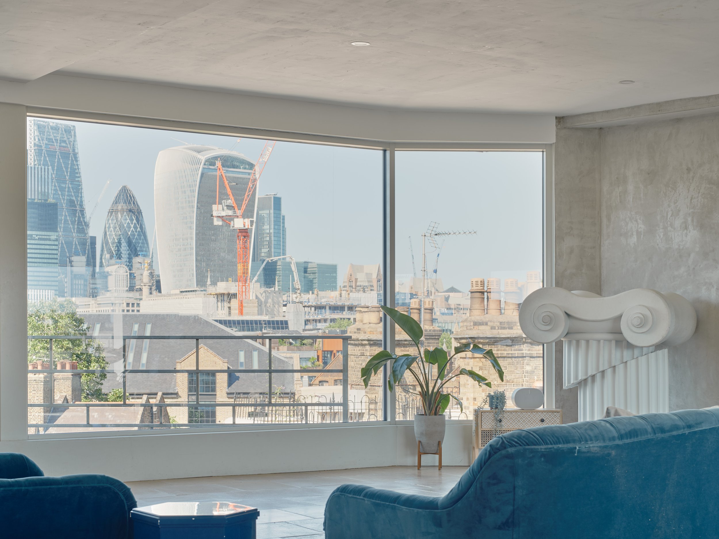 Living room with large window showing city skyline including the Gherkin and Walkie Talkie buildings, with a plant and modern decor inside.