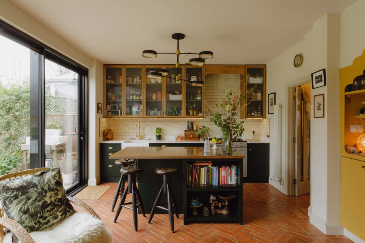 A cozy kitchen with a central island, open shelves, and large sliding glass doors leading to a garden.