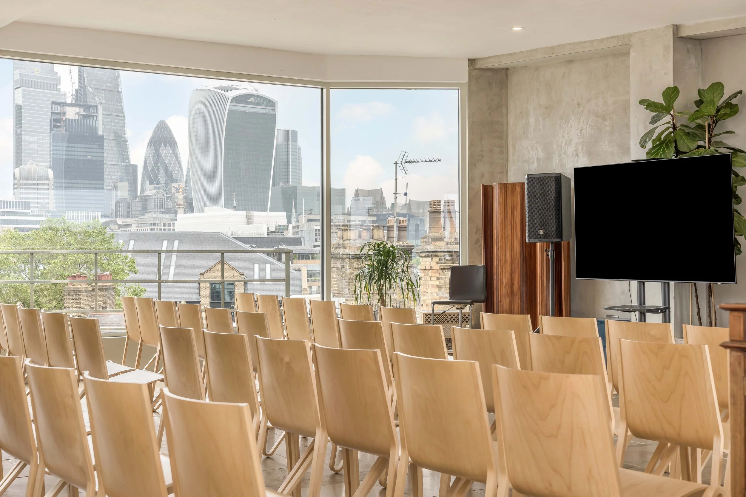 An empty conference room with wooden chairs facing a large window overlooking a city skyline with modern skyscrapers.