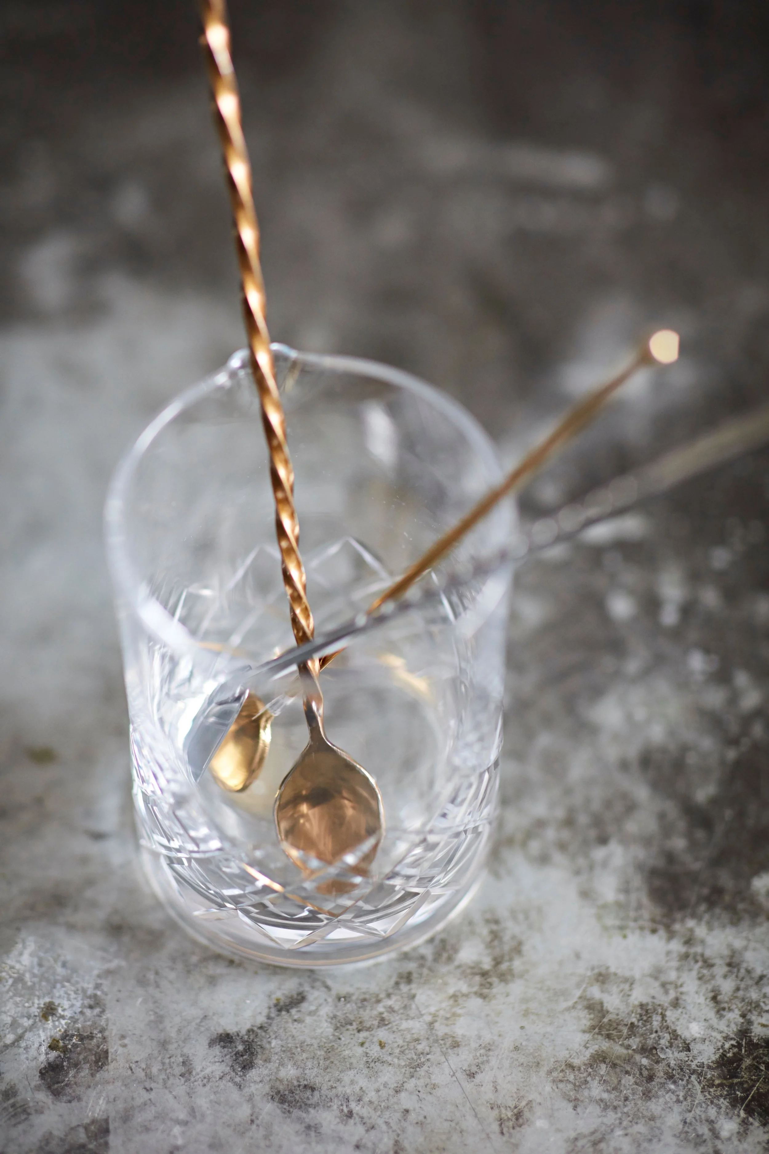 Empty crystal glass with three cocktail stirrers inside, on a textured gray surface.