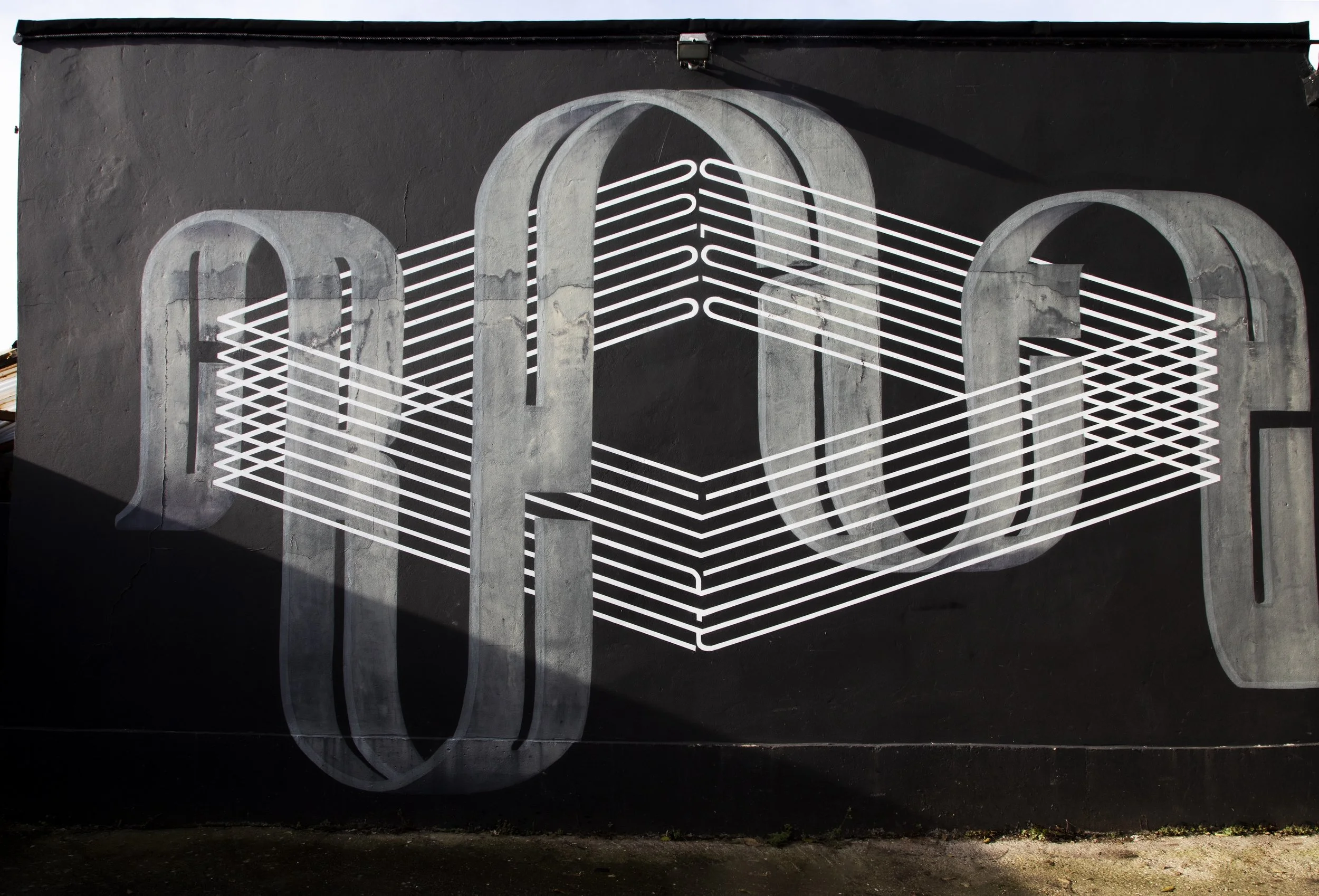 Street art mural featuring the letters 'O' and 'O' with white horizontal lines connecting them on a black wall.