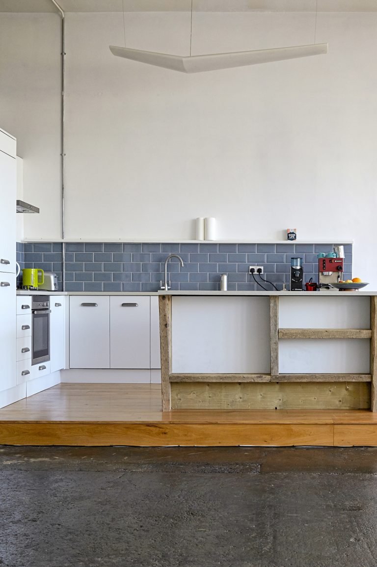 Minimalist kitchen with white cabinets, gray subway tile backsplash, a wooden countertop, and a partially constructed breakfast bar or island. Small appliances and utensils are visible on the counter.