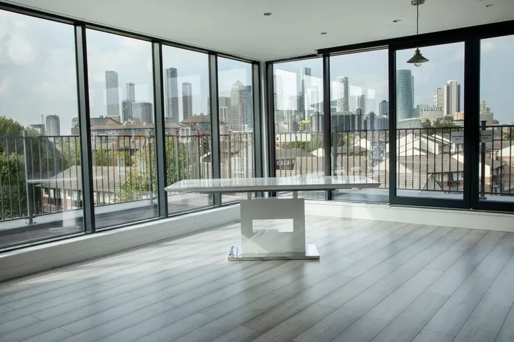 Empty room with large floor-to-ceiling windows showcasing a city skyline, with a white table in the center and a modern ceiling light fixture.