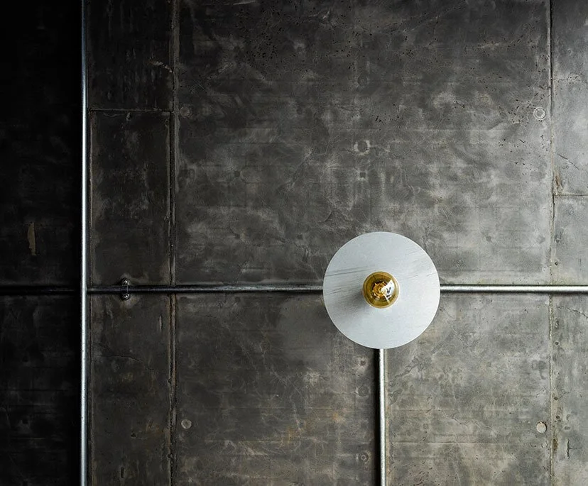 Overhead view of a concrete ceiling with metallic pipes and a hanging ceiling light with a yellowish light bulb.