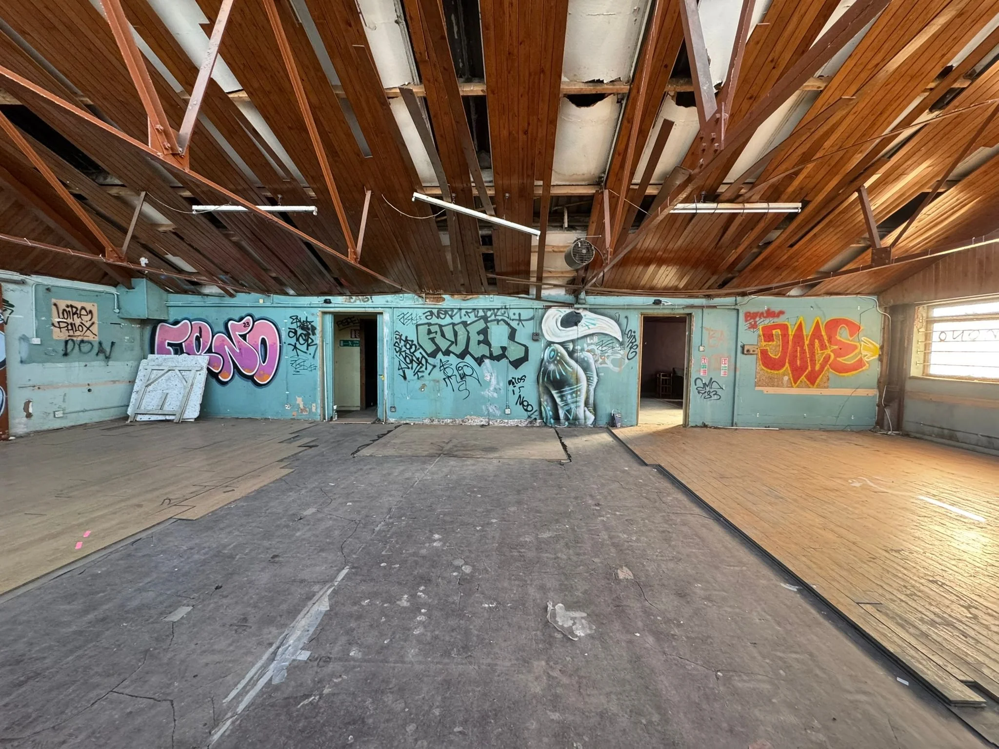 Interior of an abandoned building with a wooden ceiling, graffiti on the walls, and worn flooring.
