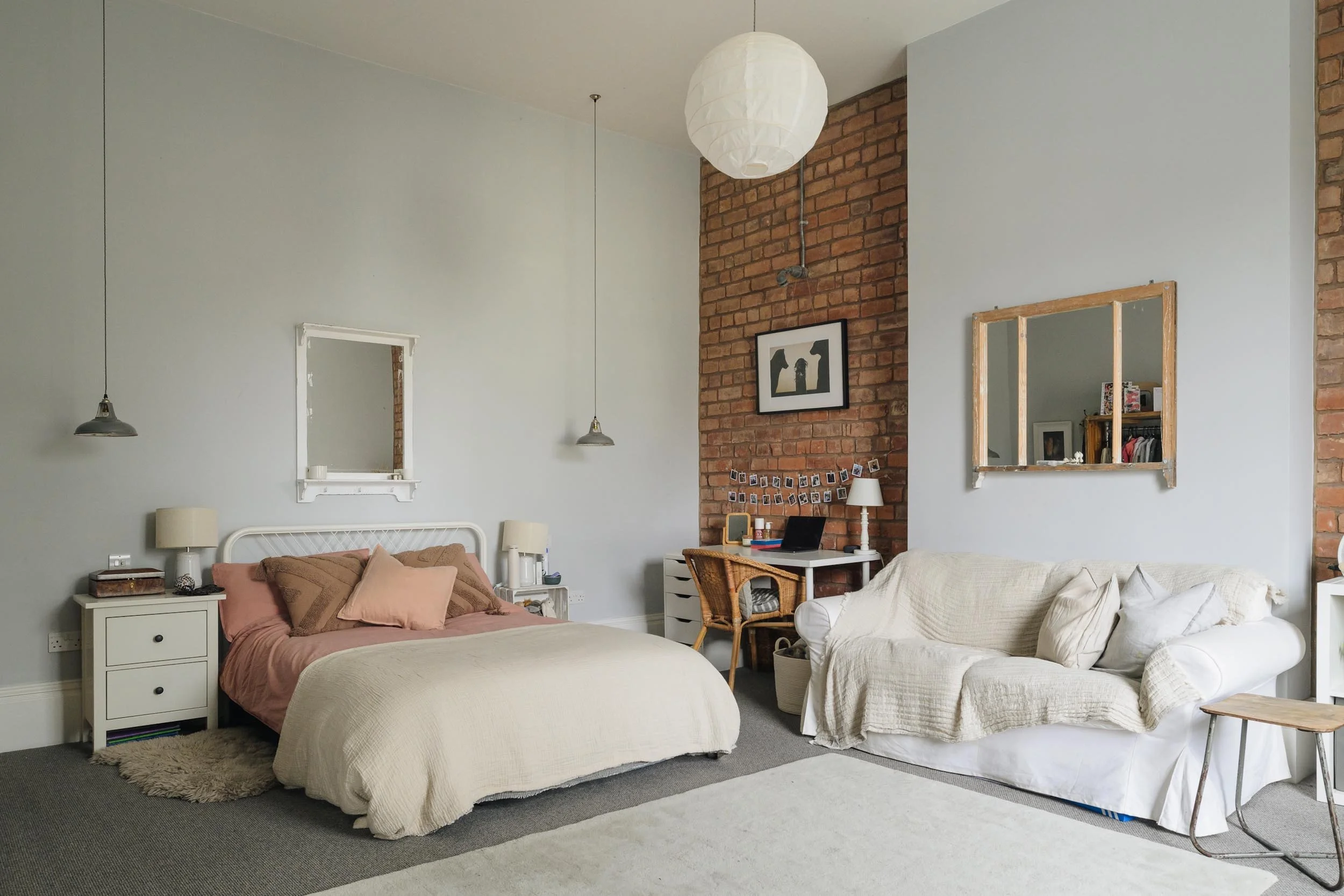 Living room with a bed, nightstands, sofas, and a brick accent wall with artwork and a desk.