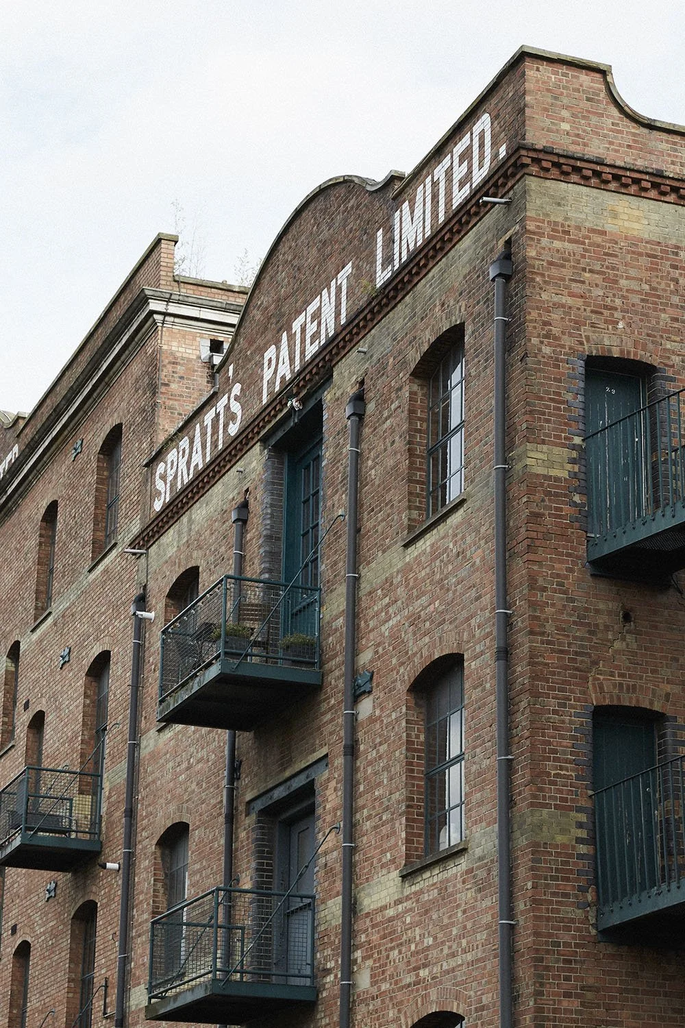 A brick building with a sign that says 'Sprats Patty Limited'. The building has green doors and small balconies with metal railings.