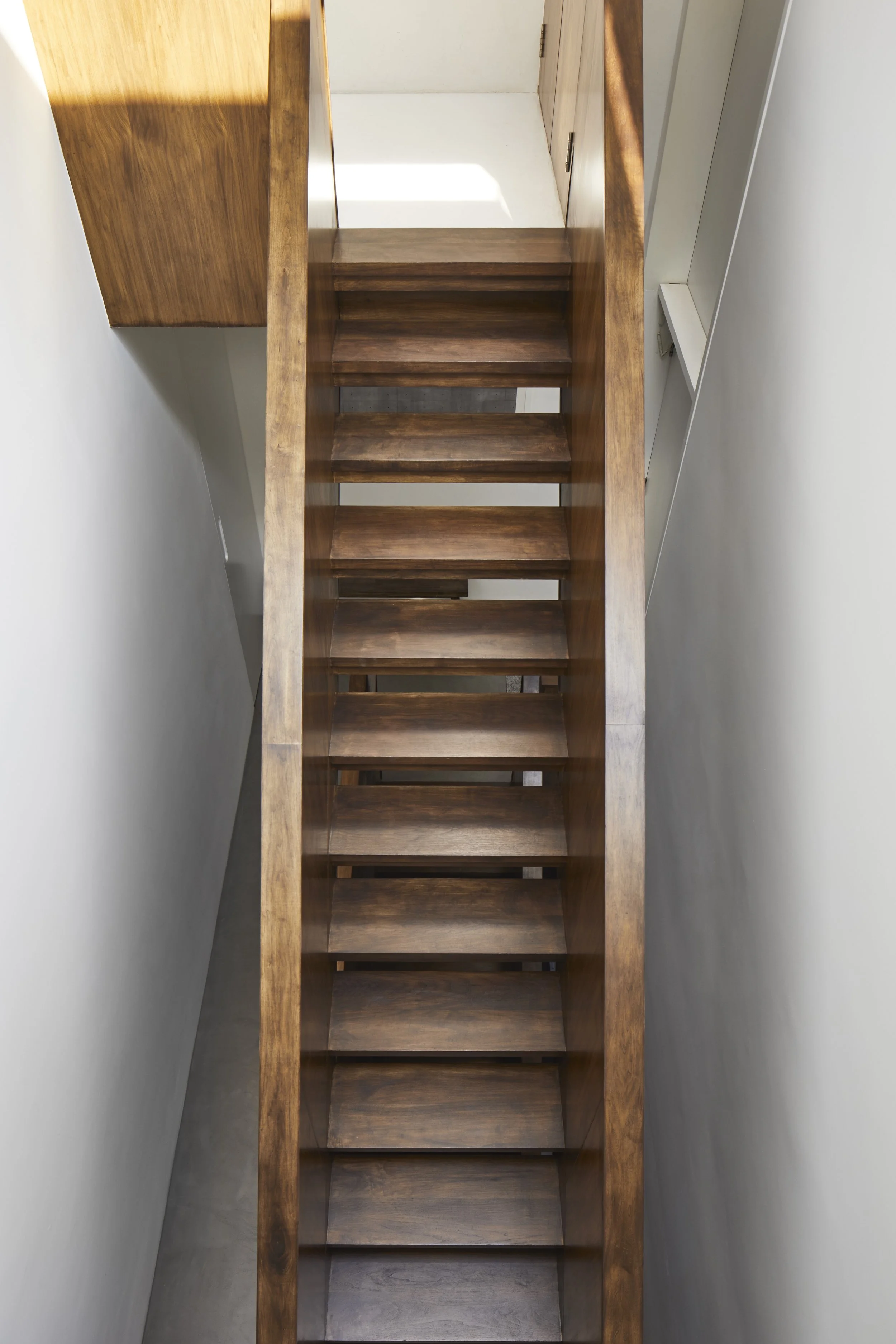 High-angle view of a wooden staircase with open risers, located between white walls.