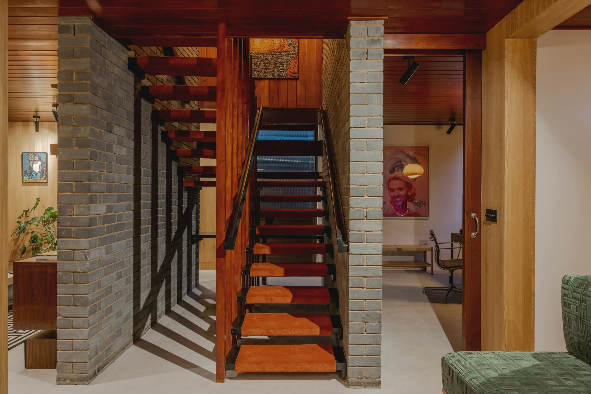 Interior view of a home with a staircase, brick and wooden walls, and framed artwork, including a portrait of a woman with blonde hair.