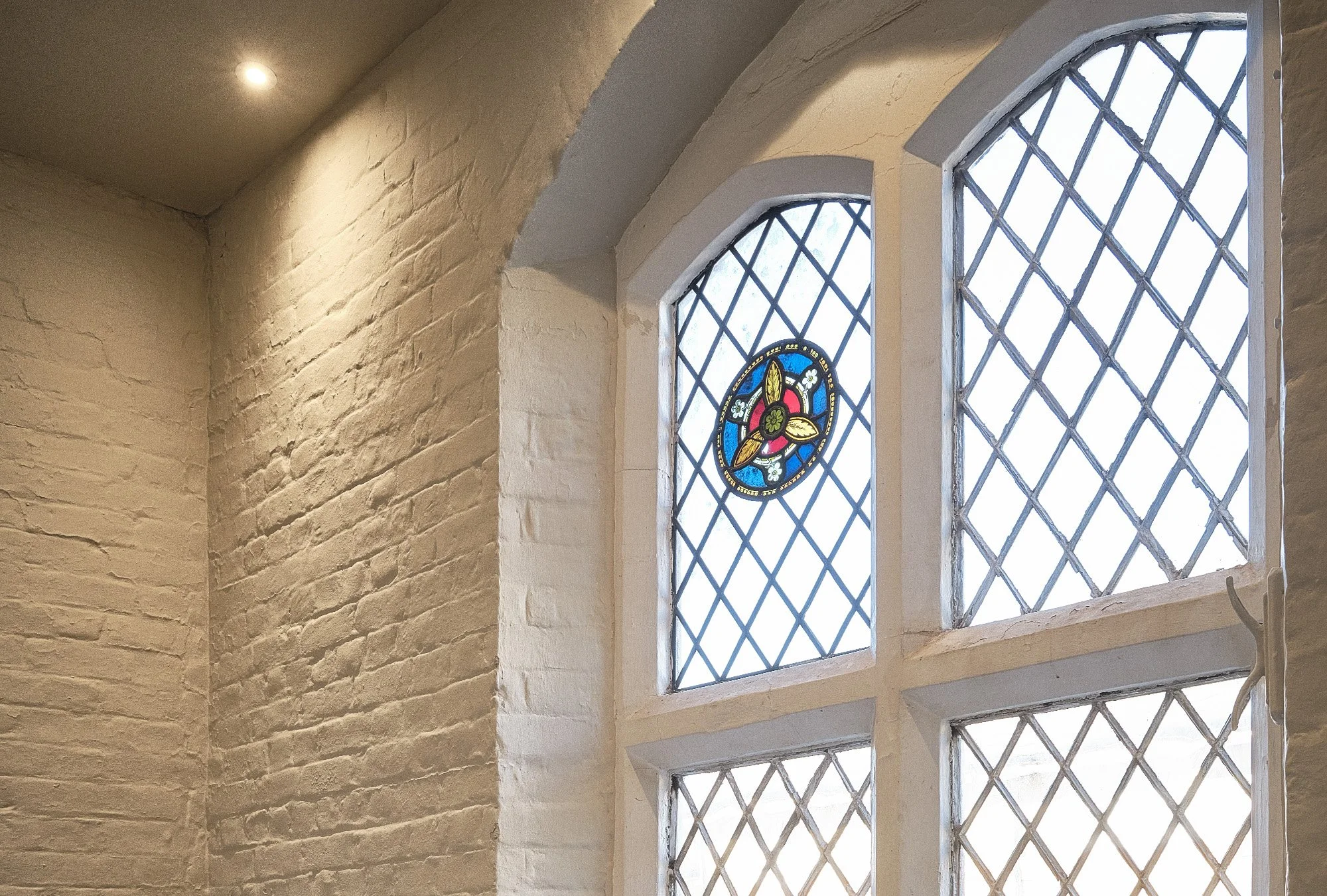 Interior view of a room with a brick wall and large stained glass windows featuring colorful designs and diamond patterns.