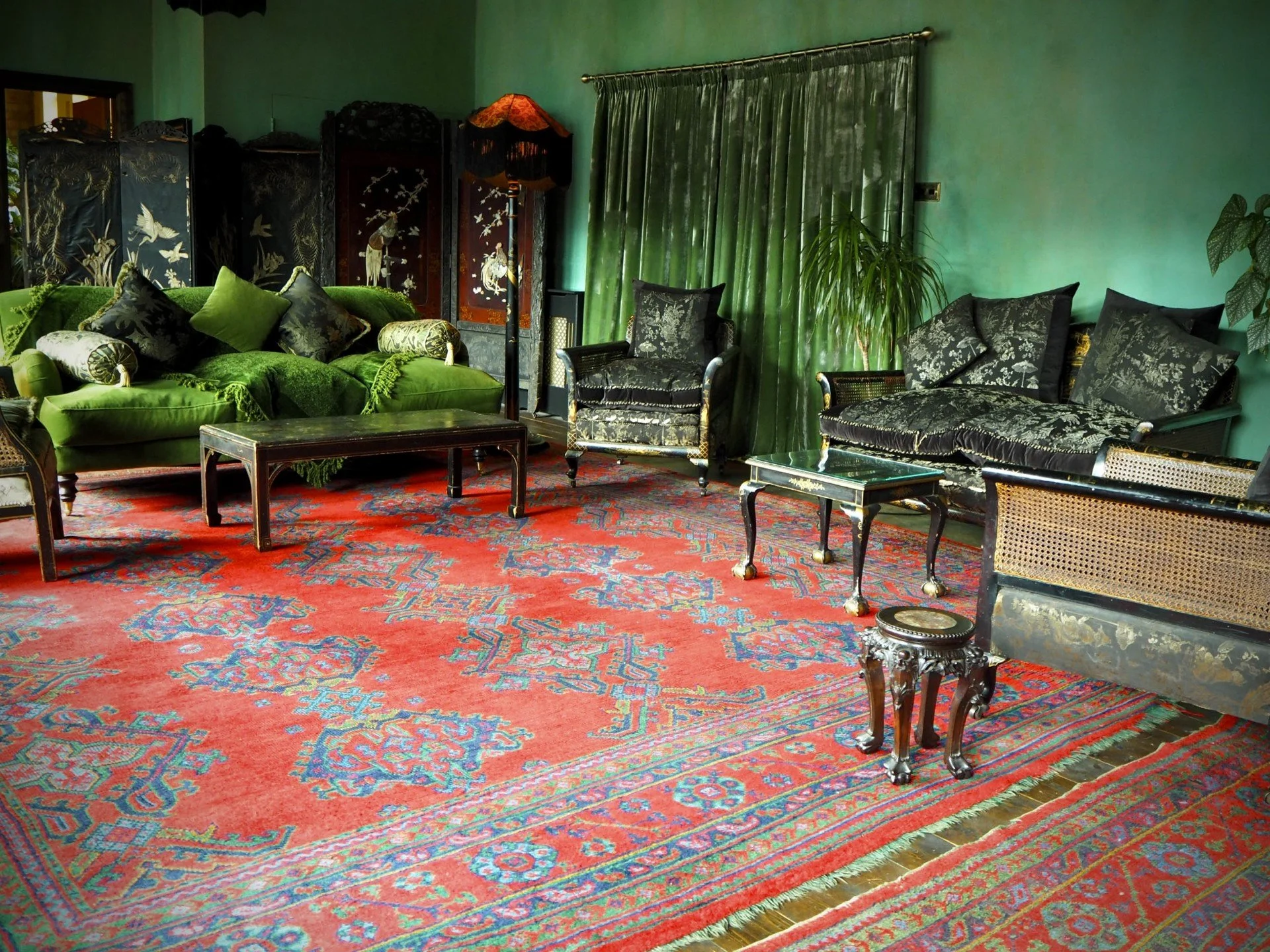 Living room with vintage furniture, green velvet sofa, black and floral-patterned chairs, Persian rug, and green walls.