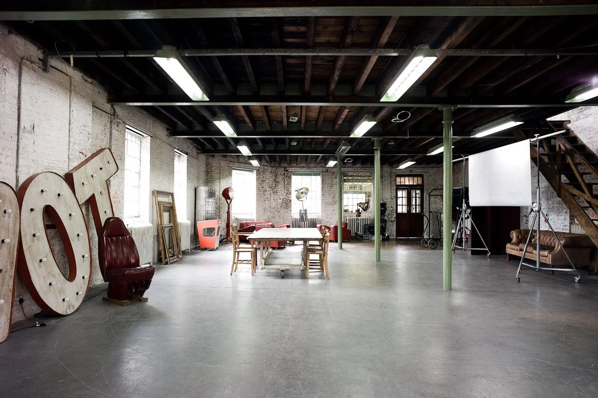 Empty industrial-style loft with vintage furniture, large illuminated letters spelling 'HOT', and film equipment.