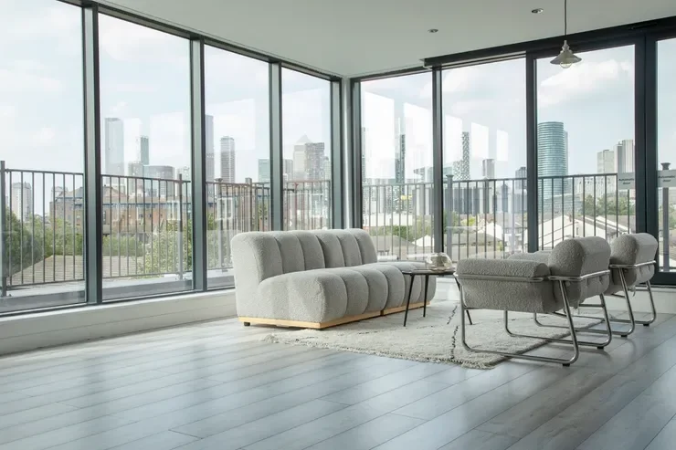 Modern living room with large floor-to-ceiling windows, a light gray sofa, a small coffee table, and two matching gray armchairs, showcasing a city skyline view.